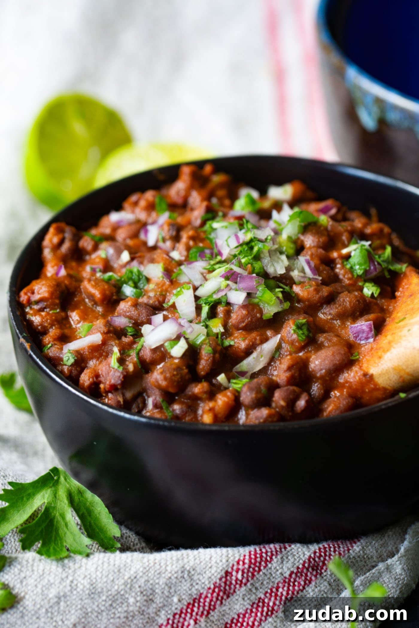 The Most Delicious Mexican Black Beans Ever A wooden spoon scoops a generous portion of flavorful Mexican black beans, garnished with red onion and cilantro, from a rustic bowl.