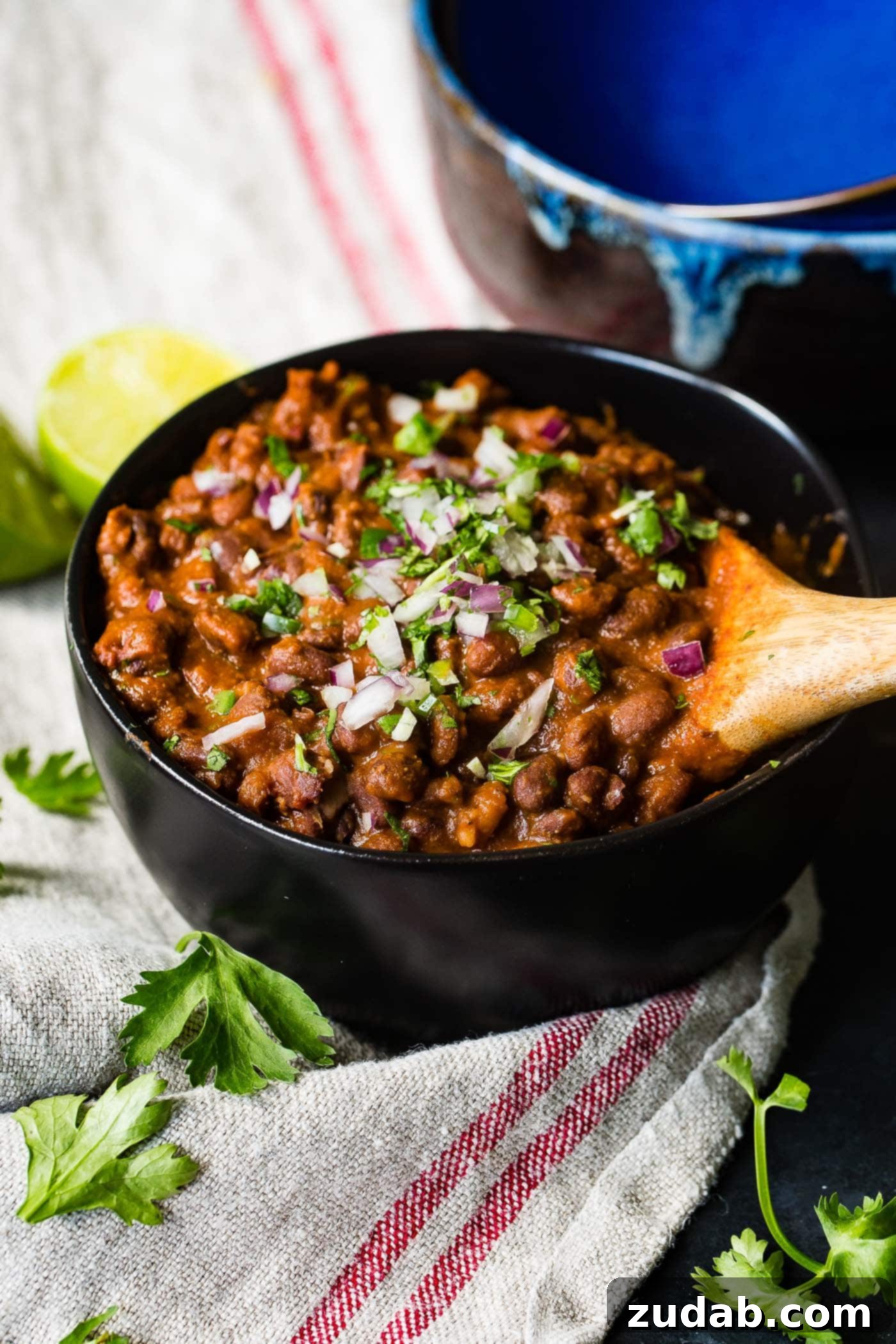 The Most Delicious Mexican Black Beans Ever Another enticing close-up of Mexican black beans in a bowl, being served with a wooden spoon, highlighting their rich texture and appealing garnishes.