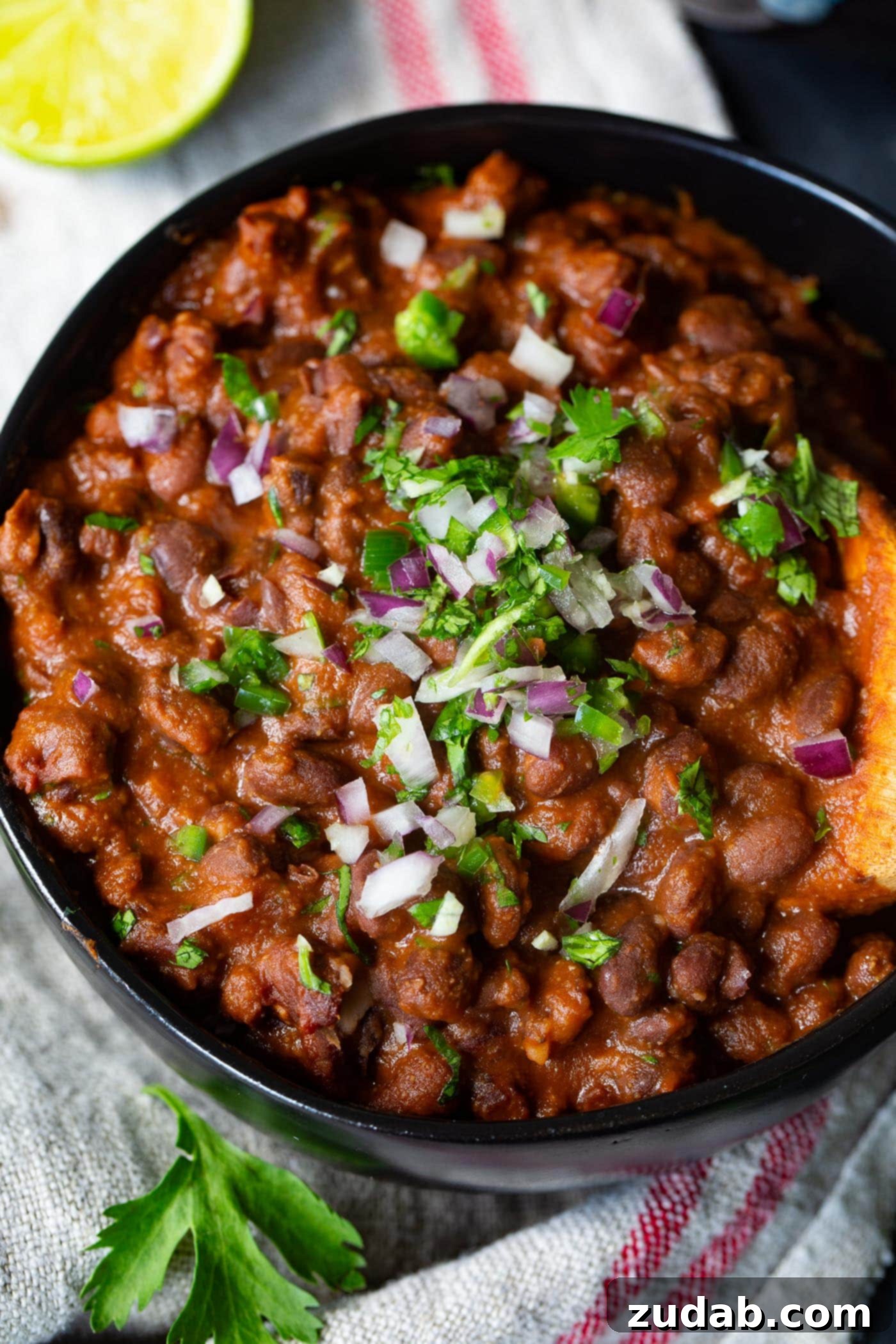 The Most Delicious Mexican Black Beans Ever A tantalizing overhead shot of Mexican black beans, artfully garnished with fresh cilantro and red onion, being scooped from a bowl with a wooden utensil.