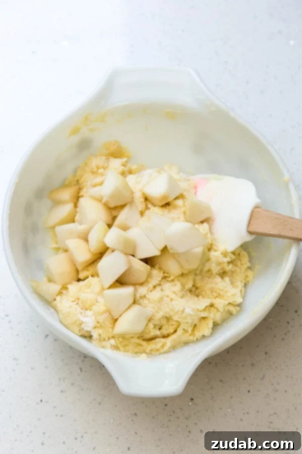 Classic Italian Pear Almond Cake 3 Hands gently folding diced fresh pears into a creamy cake batter in a large mixing bowl, ensuring even distribution.