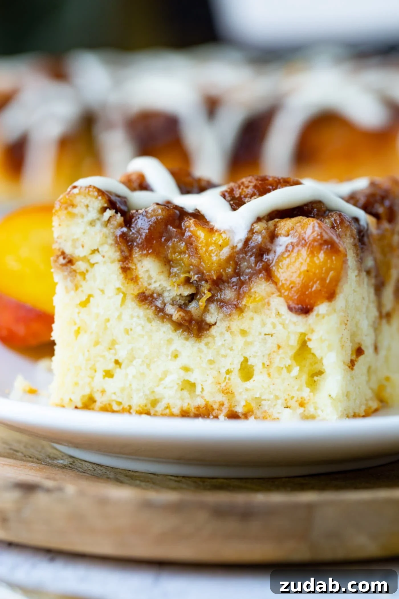 Easy Peach Sour Cream Coffee Cake A delectable slice of peach sour cream coffee cake, generously topped with a rich brown sugar peach topping and a sweet vanilla glaze, rests on a pristine white plate, accompanied by a rustic wooden board.