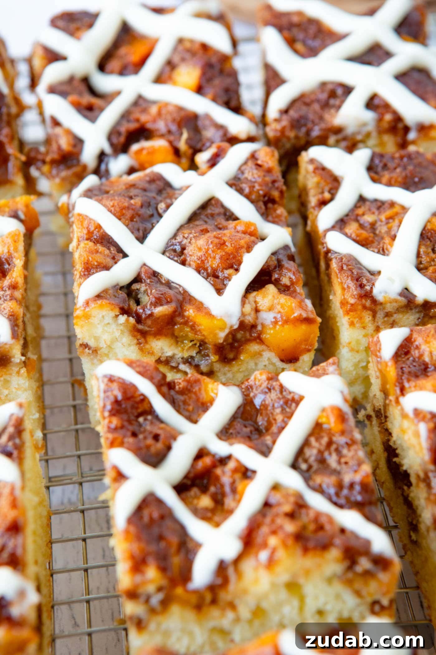 Easy Peach Sour Cream Coffee Cake Several slices of golden-brown peach coffee cake, each adorned with a generous swirl of sweet glaze, are beautifully arranged, showcasing the inviting texture and vibrant peach filling.