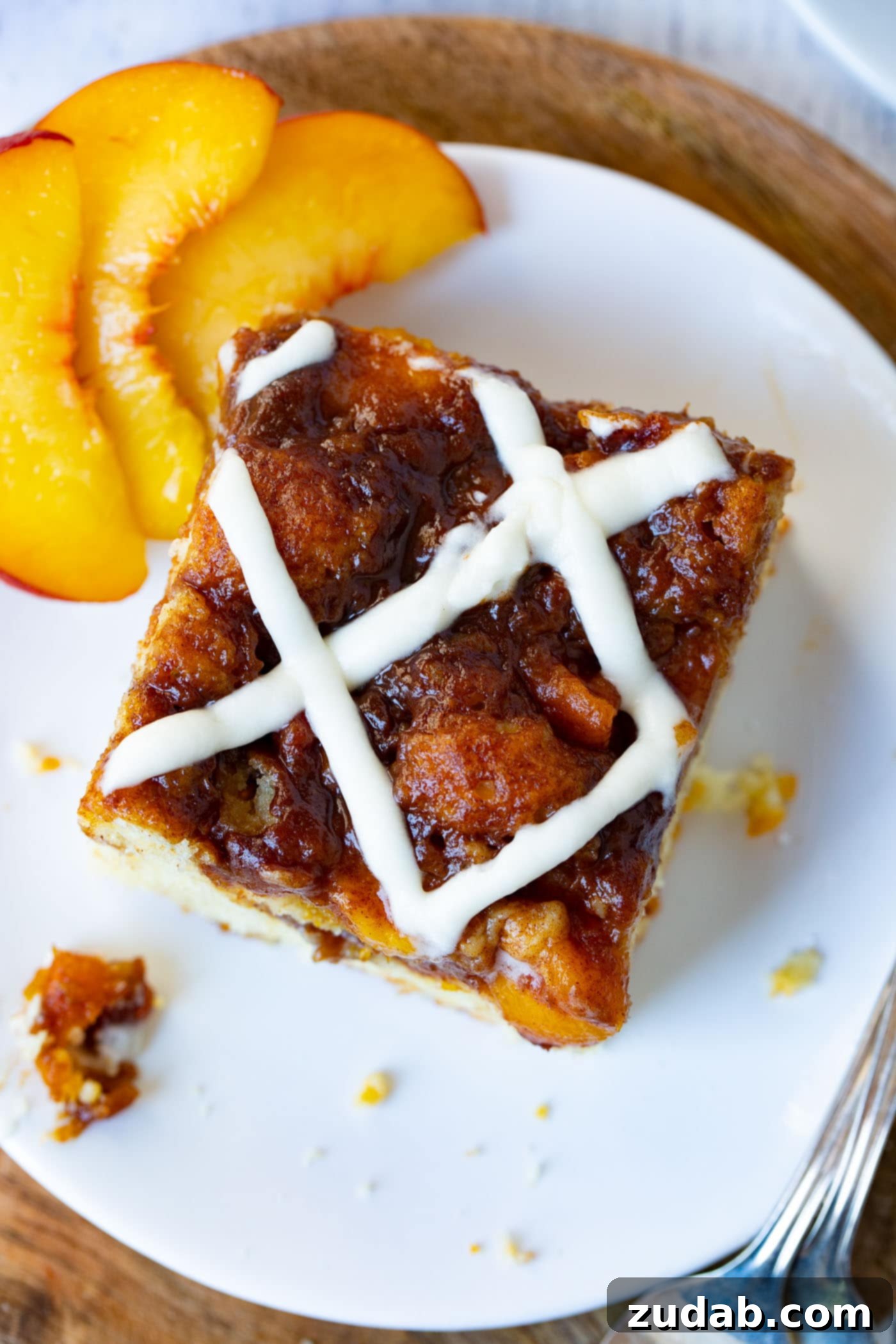 Easy Peach Sour Cream Coffee Cake A single, inviting piece of peach coffee cake, exquisitely glazed and garnished with fresh peach slices, rests on a white plate, ready to be enjoyed.