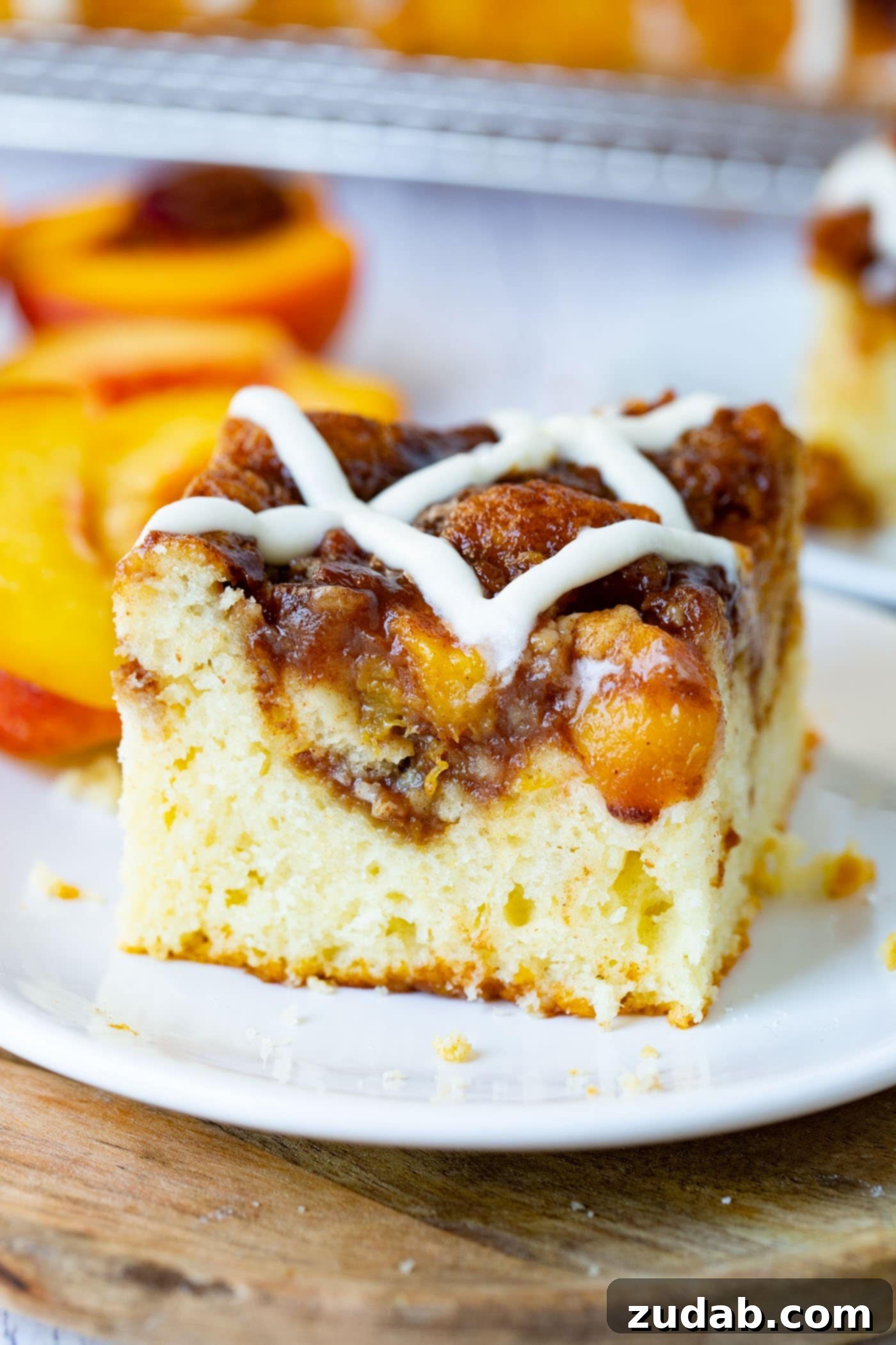 Easy Peach Sour Cream Coffee Cake A close-up photograph of a single, delectable piece of peach coffee cake, featuring a glistening sweet glaze and the soft, inviting texture of the cake on a crisp white plate.