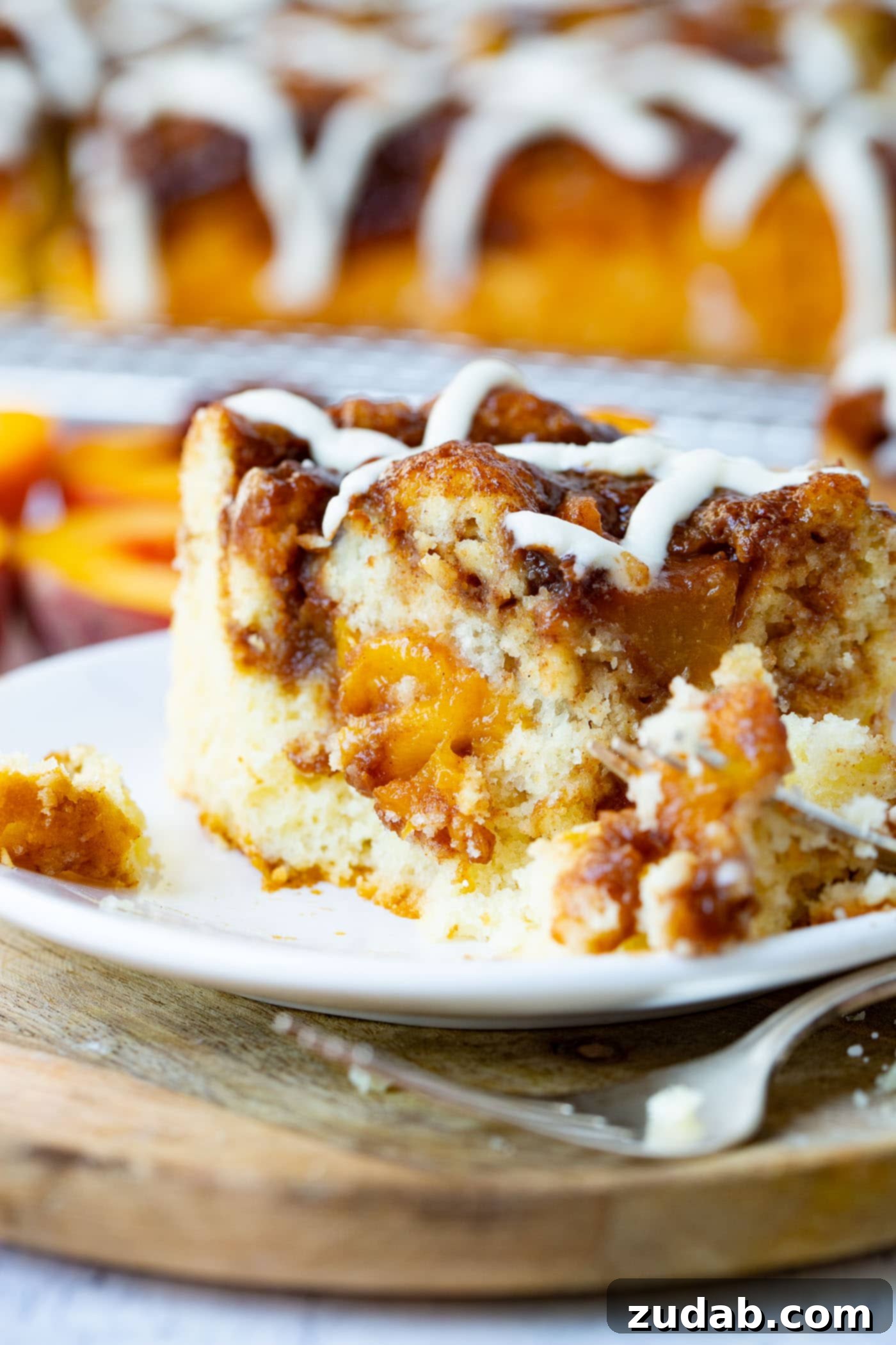 Easy Peach Sour Cream Coffee Cake A beautifully composed image of a single slice of peach coffee cake on a white plate, with a fork gently cutting into it, revealing the tender, fruity interior.