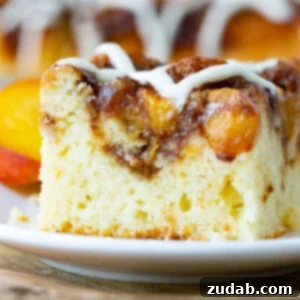 A beautifully composed close-up of a slice of Sour Cream Peach Coffee Cake, showcasing its moist texture, peach swirl, and delicate glaze.