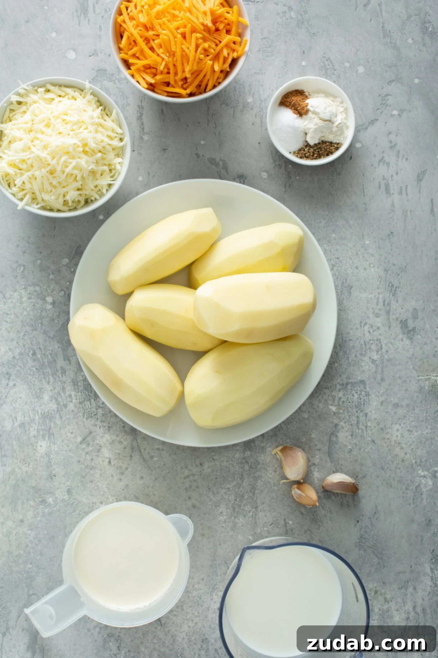 Simple Instant Pot Cheesy Potatoes A bowl of six peeled potatoes. There are small containers of grated cheese,