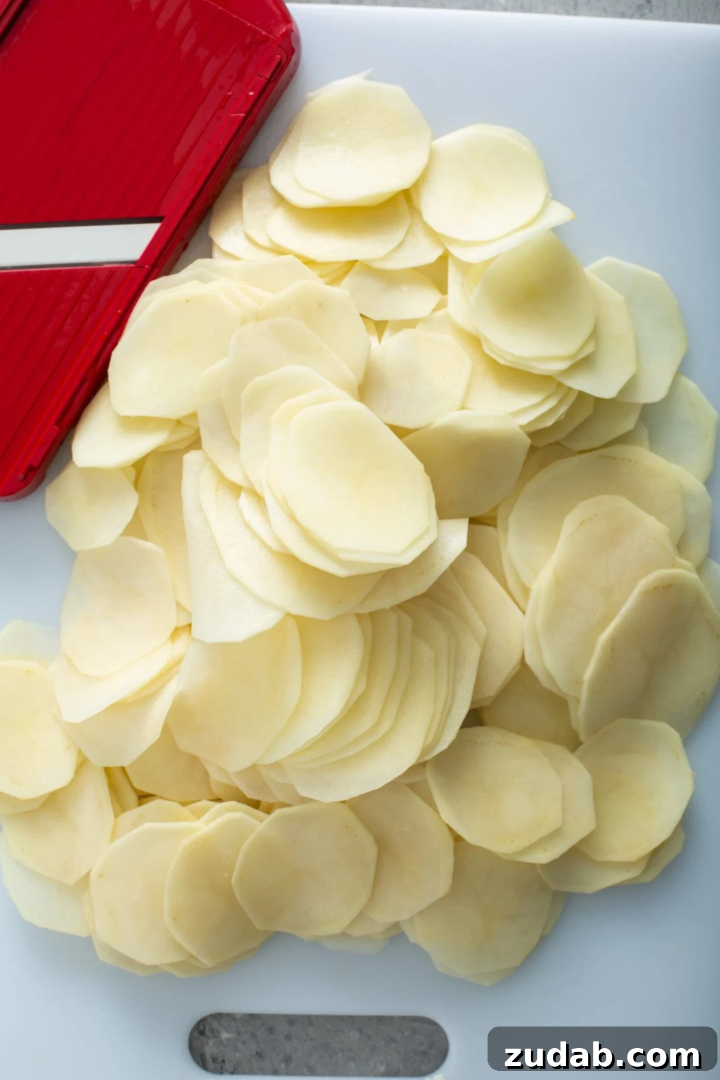 Simple Instant Pot Cheesy Potatoes Raw, peeled, sliced potatoes with a red and white kitchen towel in the background.