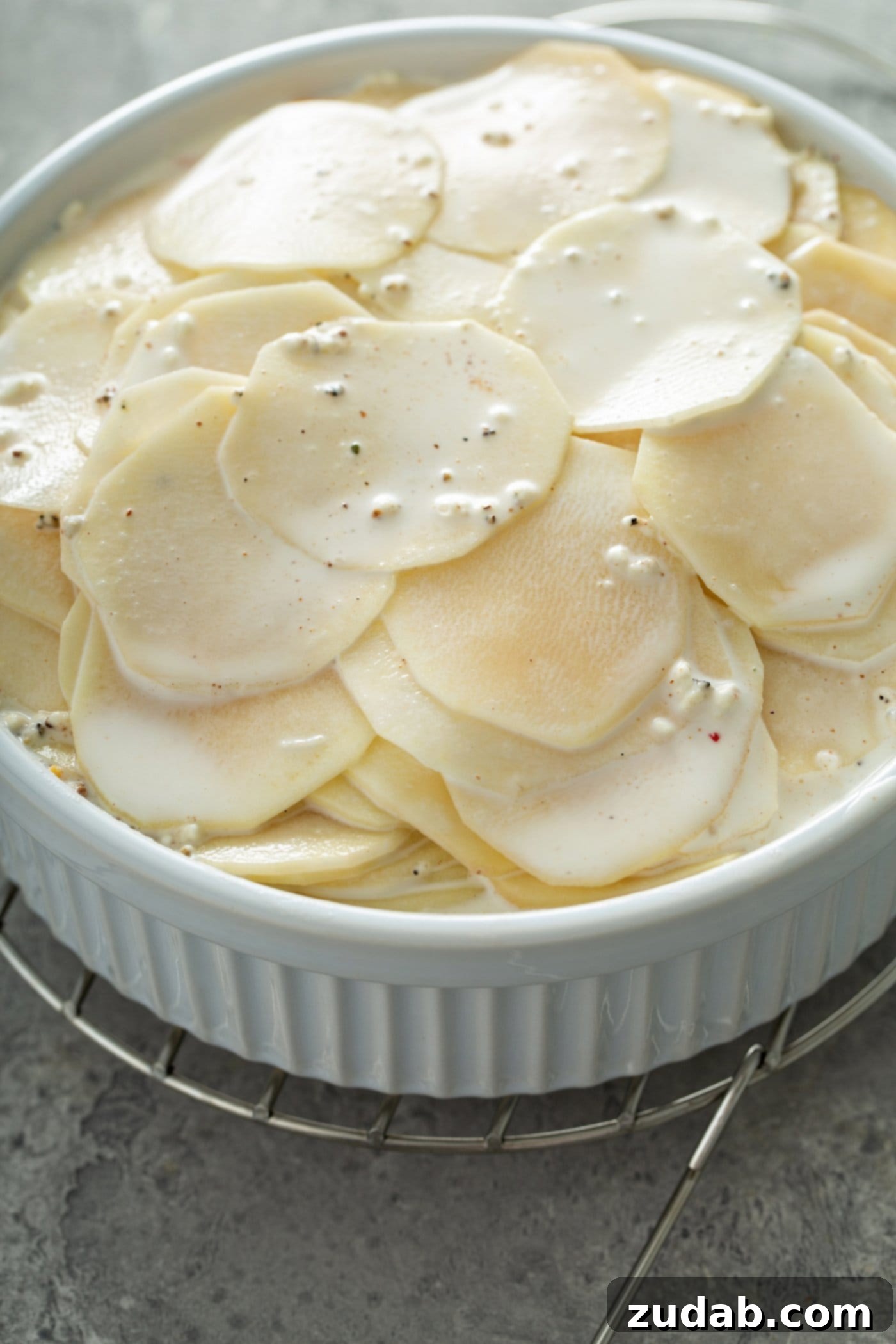 Simple Instant Pot Cheesy Potatoes A casserole dish filled with sliced raw potatoes. A cream sauce is poured over the top.