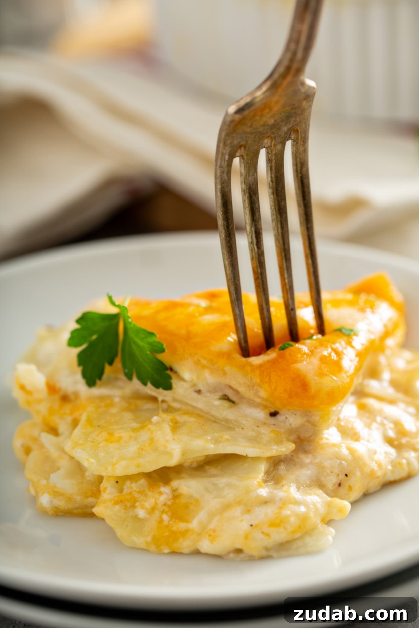 Simple Instant Pot Cheesy Potatoes A serving of instant pot potatoes with a leaf of parsley on top. A fork is piercing the melted cheese on top of the potatoes. There is a white linen napkin in the background.