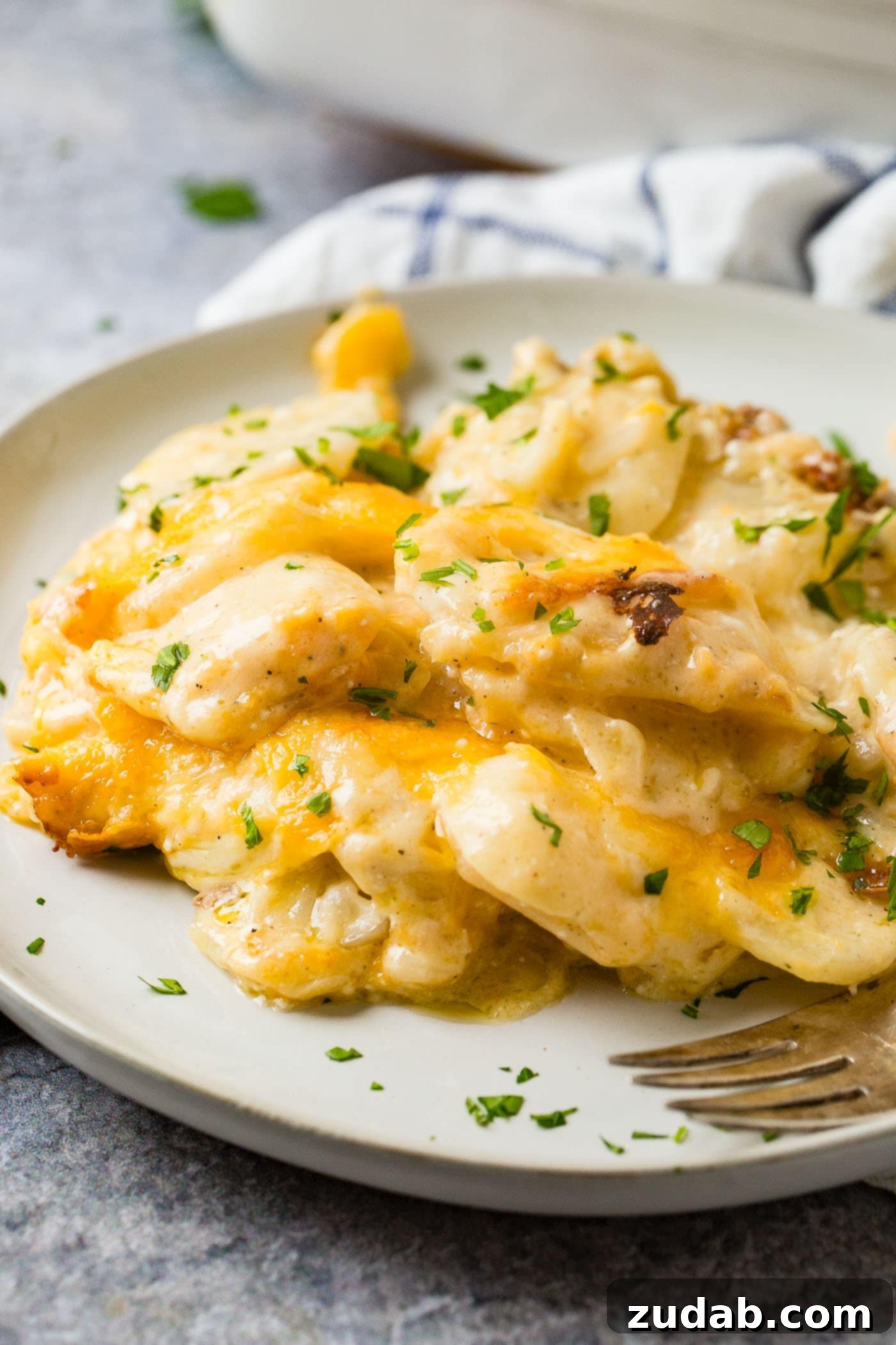 The Best Cheesy Potato Casserole Side Dish 3 a gray plate loaded with cheesy potato casserole and a sprinkling of parsley