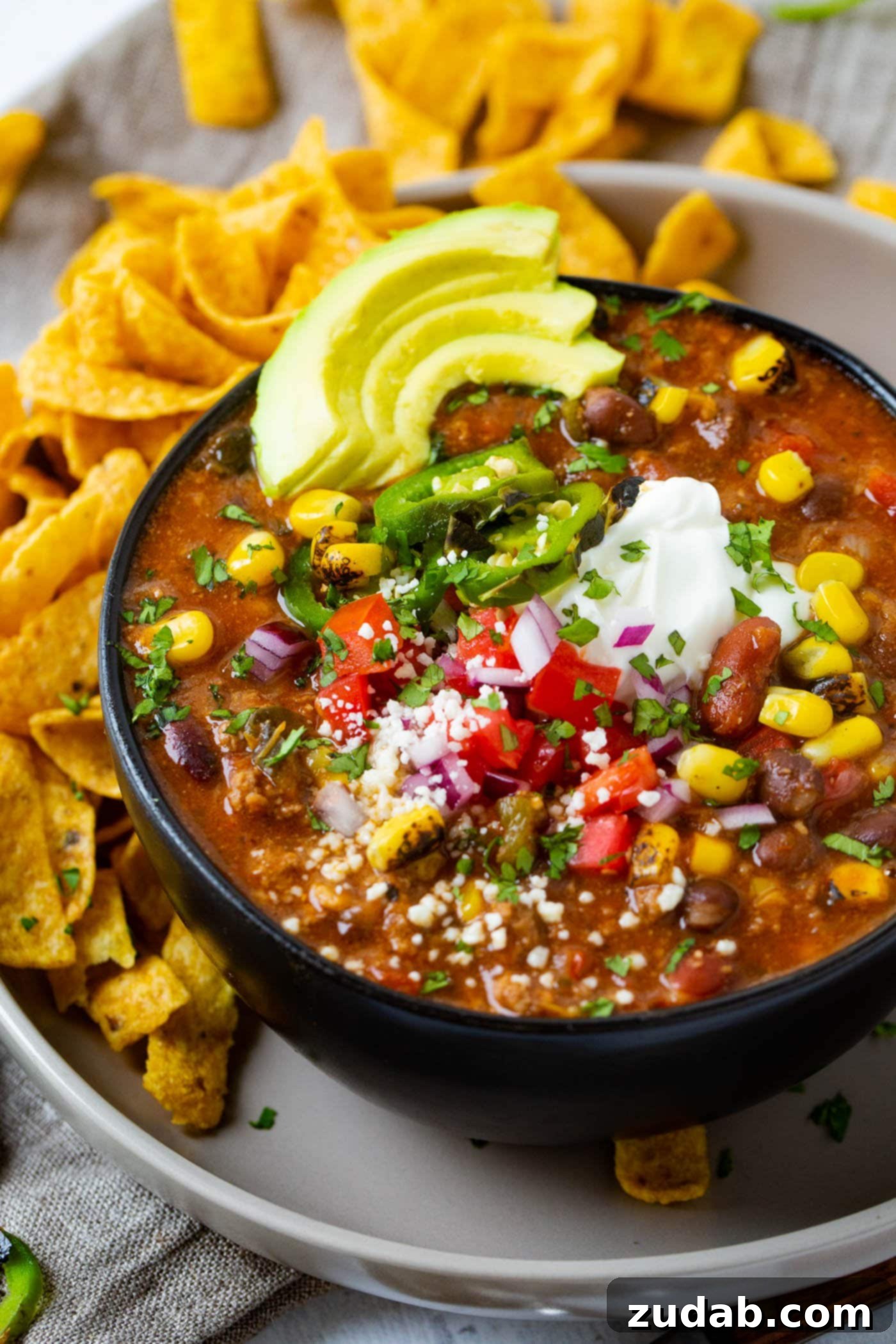 Easy Instant Pot Taco Ground Beef Chili 2 A vibrant bowl of Taco Ground Beef Instant Pot Chili, garnished with fresh corn, creamy avocados, and crunchy Fritos chips, presented on a stylish gray plate.