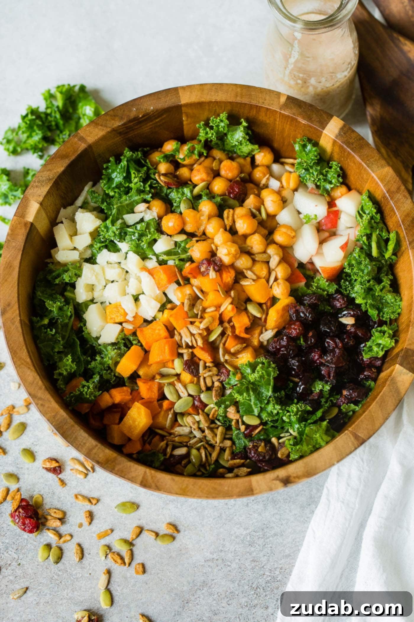 Winter Roasted Butternut Squash Kale Salad A photo of a large wooden bowl full of kale salad topped with roasted butternut squash, craisins, chickpeas, pepitas, apples and gouda cheese.