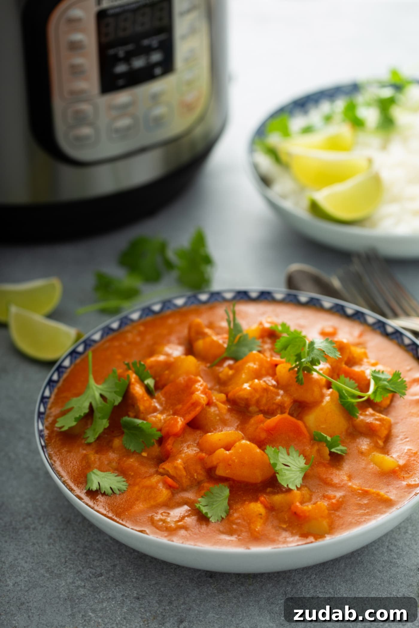 Chicken Curry Recipe in the Instant Pot A bowl of chicken curry with chunks of chicken, potatoes and carrots in a curry sauce. Fresh parsley leaves are sprinkled on top and there is an instant pot, and lime wedges in the background.