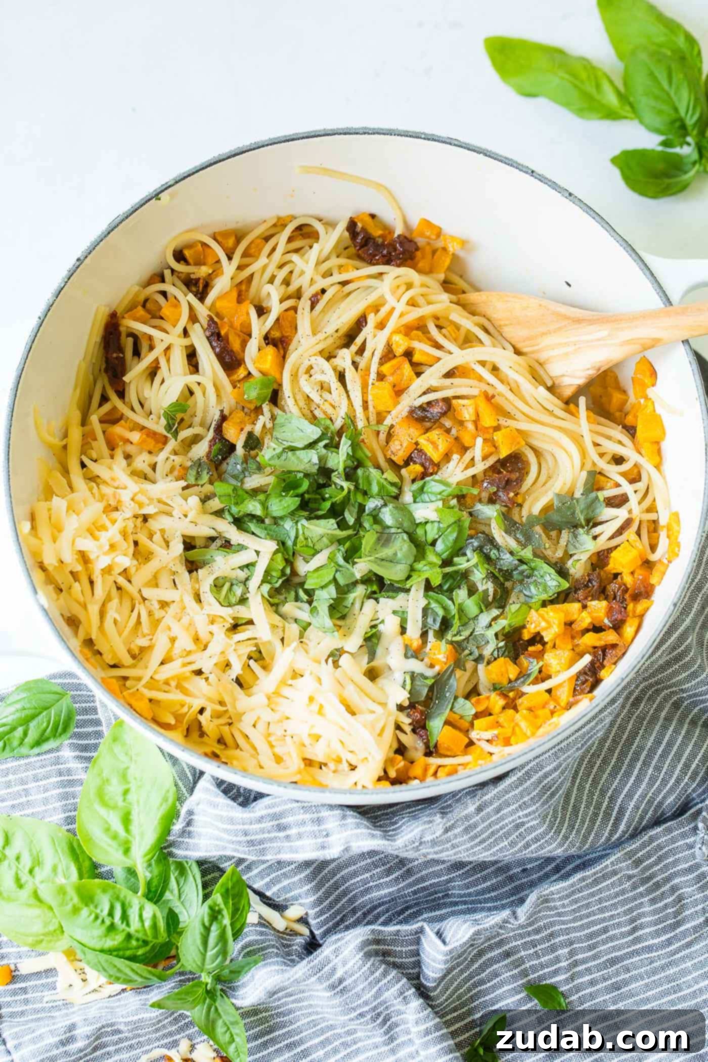 25 Minute Vegetarian Butternut Squash Pasta A close-up photo of a large pot brimming with cooked spaghetti, generously mixed with vibrant ingredients: golden roasted butternut squash, bright red sun-dried tomatoes, aromatic green basil leaves, and creamy melted cheese. The colors are rich and inviting.