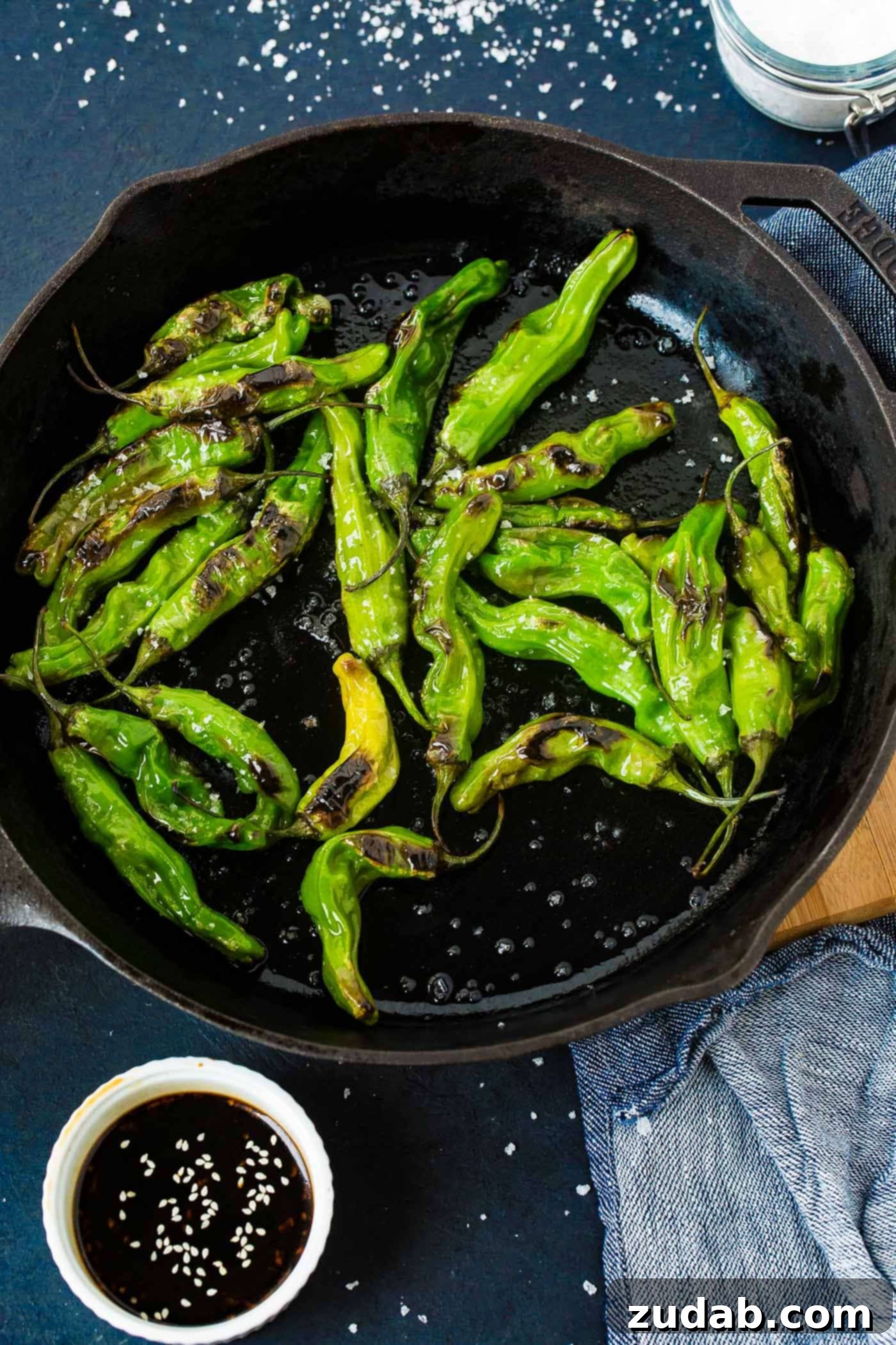 How to Get Perfectly Blistered Shishito Peppers 3 A second close-up view of the black cast iron pan, showcasing the beautifully charred and blistered bright green shishito peppers, ready to be seasoned with flaked sea salt.