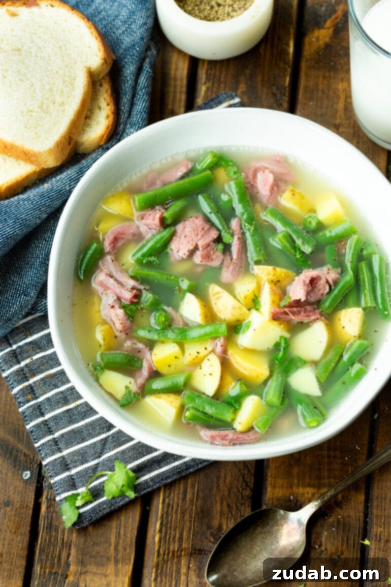 Wholesome Ham Hock Soup: Hearty and Nutritious 3 A photo taken over the top of a large bowl of ham hock soup loaded with cubed potatoes, green beans and chunks of ham, ready to be enjoyed.