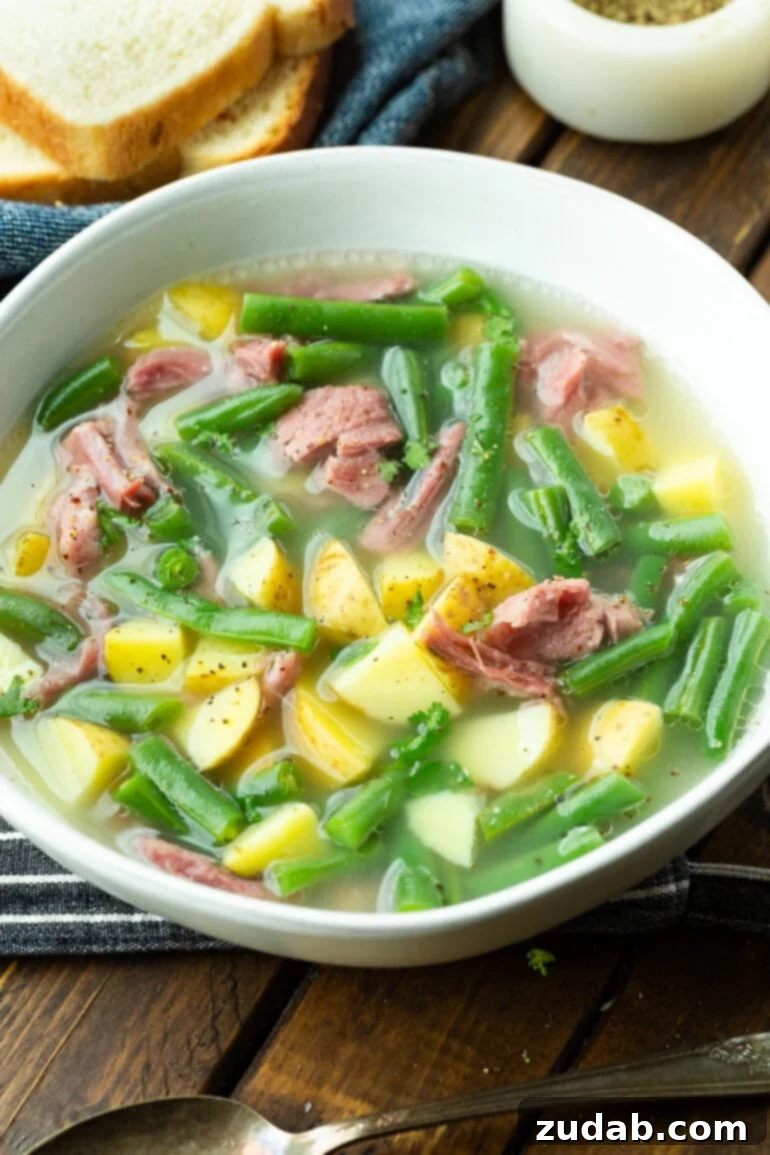 Wholesome Ham Hock Soup: Hearty and Nutritious 4 A photo of a white bowl full of ham hock soup, showcasing generous chunks of potato, ham, and green beans, inviting you to take a spoonful.