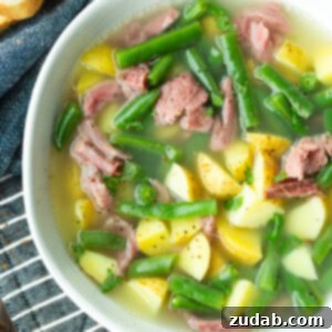A photo of a bowl of ham hock soup loaded with potatoes, green beans and chunks of ham, a perfect hearty meal.