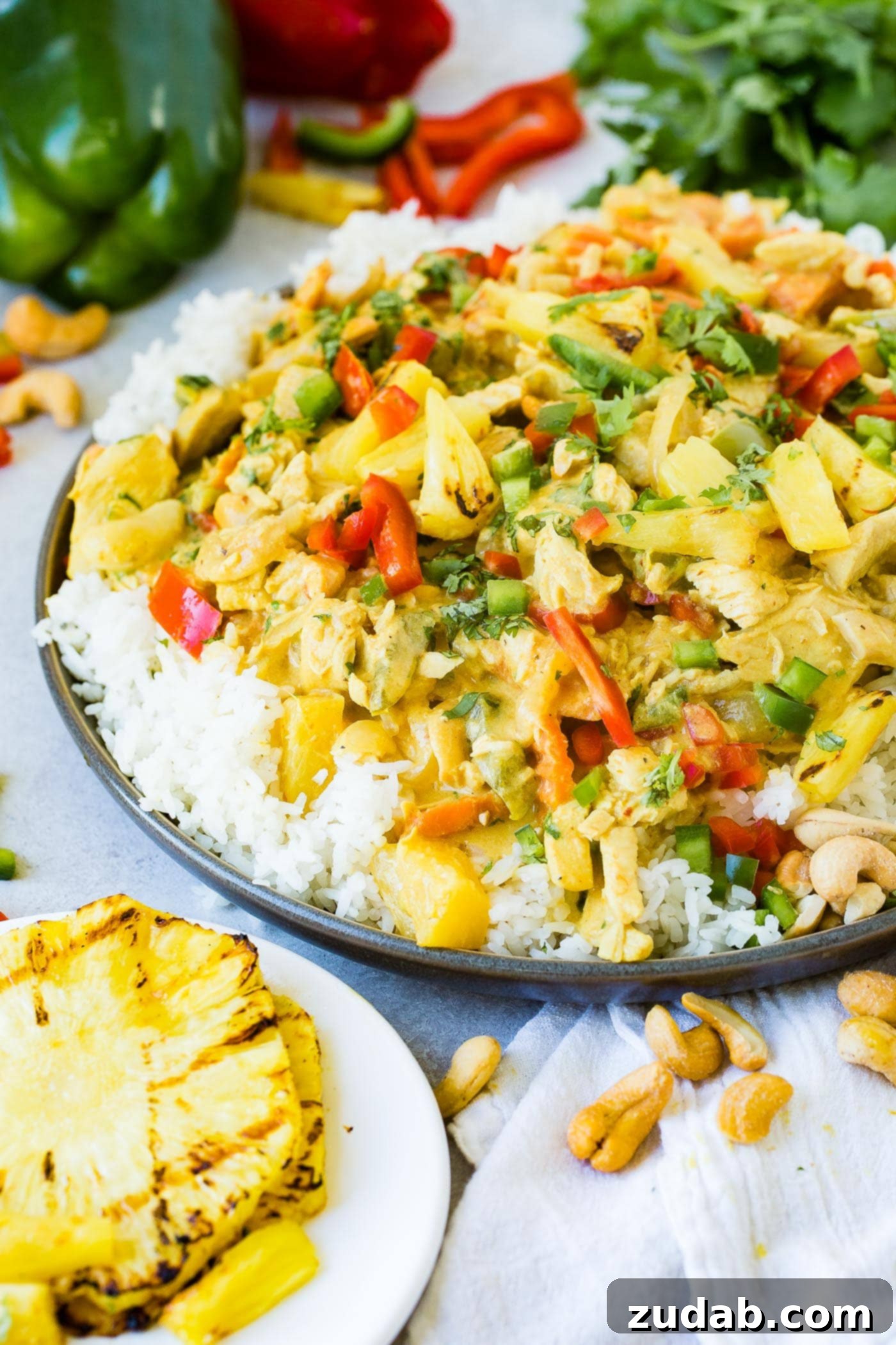 Golden Island Pineapple Coconut Chicken Curry 2 a plate with jasmine white rice piled with a creamy pineapple coconut curry sauce, peppers, onions and cashews with grilled pineapple