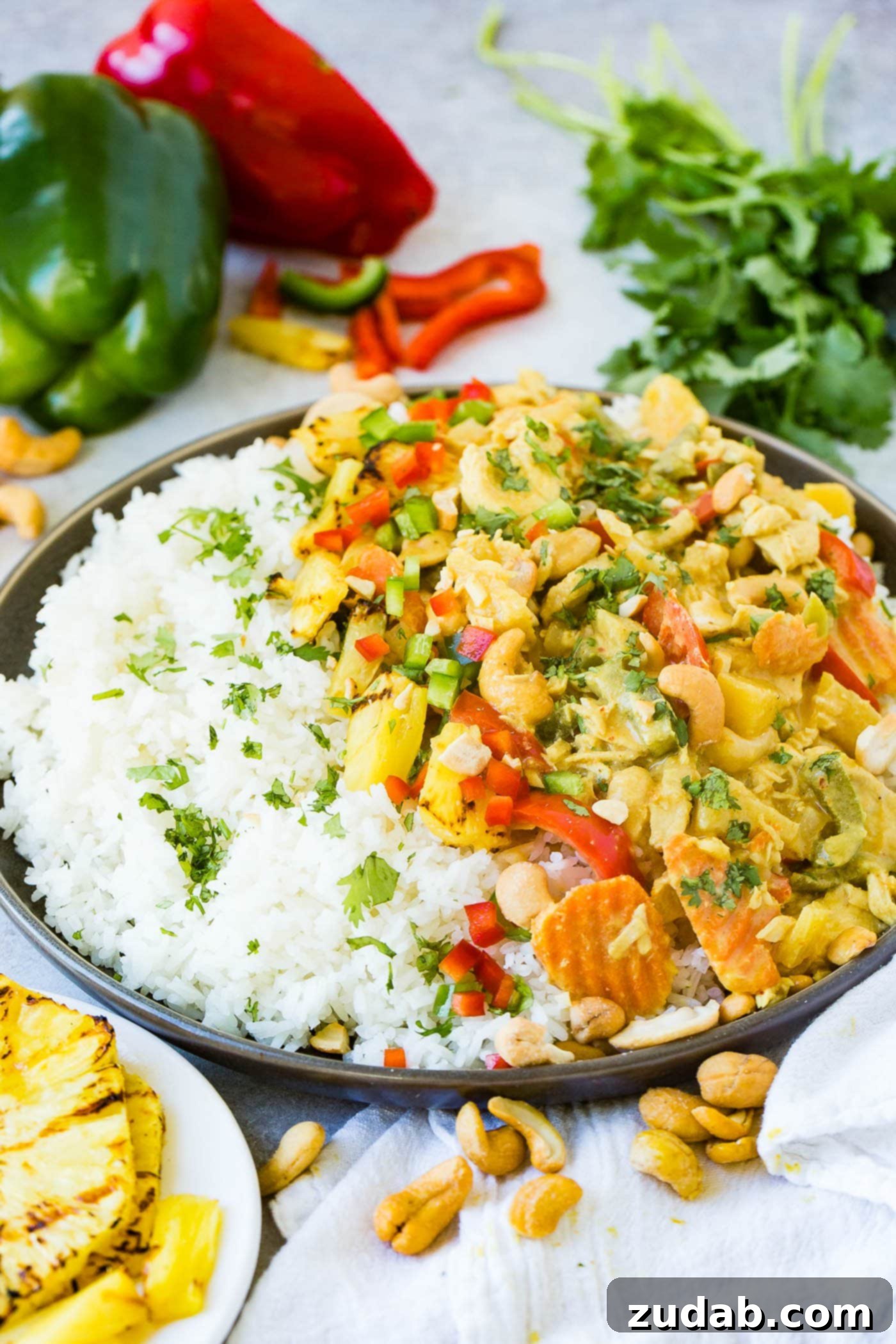 Golden Island Pineapple Coconut Chicken Curry 6 a plate with jasmine white rice piled with a creamy pineapple coconut curry sauce, peppers, onions and cashews with grilled pineapple