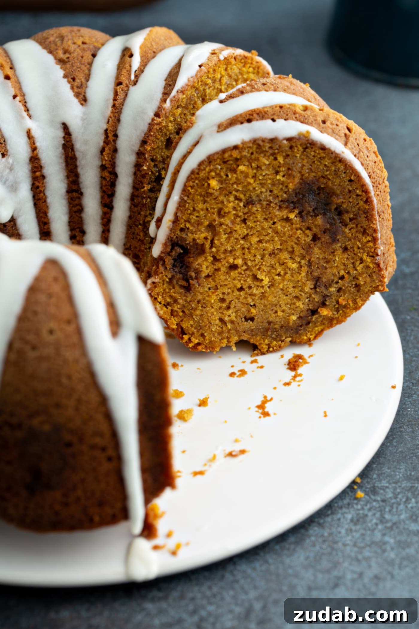 Sour Cream Cinnamon Swirl Pumpkin Bundt Cake A Sour Cream Cinnamon Swirl Pumpkin Bundt Cake, with a few slices already removed, revealing its moist interior and the inviting cinnamon swirl. The cake's top is elegantly drizzled with a white glaze, enhancing its visual appeal.