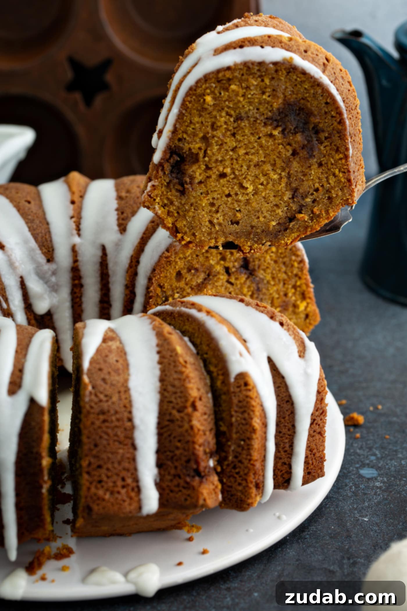 Sour Cream Cinnamon Swirl Pumpkin Bundt Cake A luscious Sour Cream Cinnamon Swirl Pumpkin Bundt Cake, adorned with a delicate drizzle of glaze, being served. A cake server carefully removes a slice, clearly revealing the rich, enticing cinnamon swirl embedded within the moist cake layers.