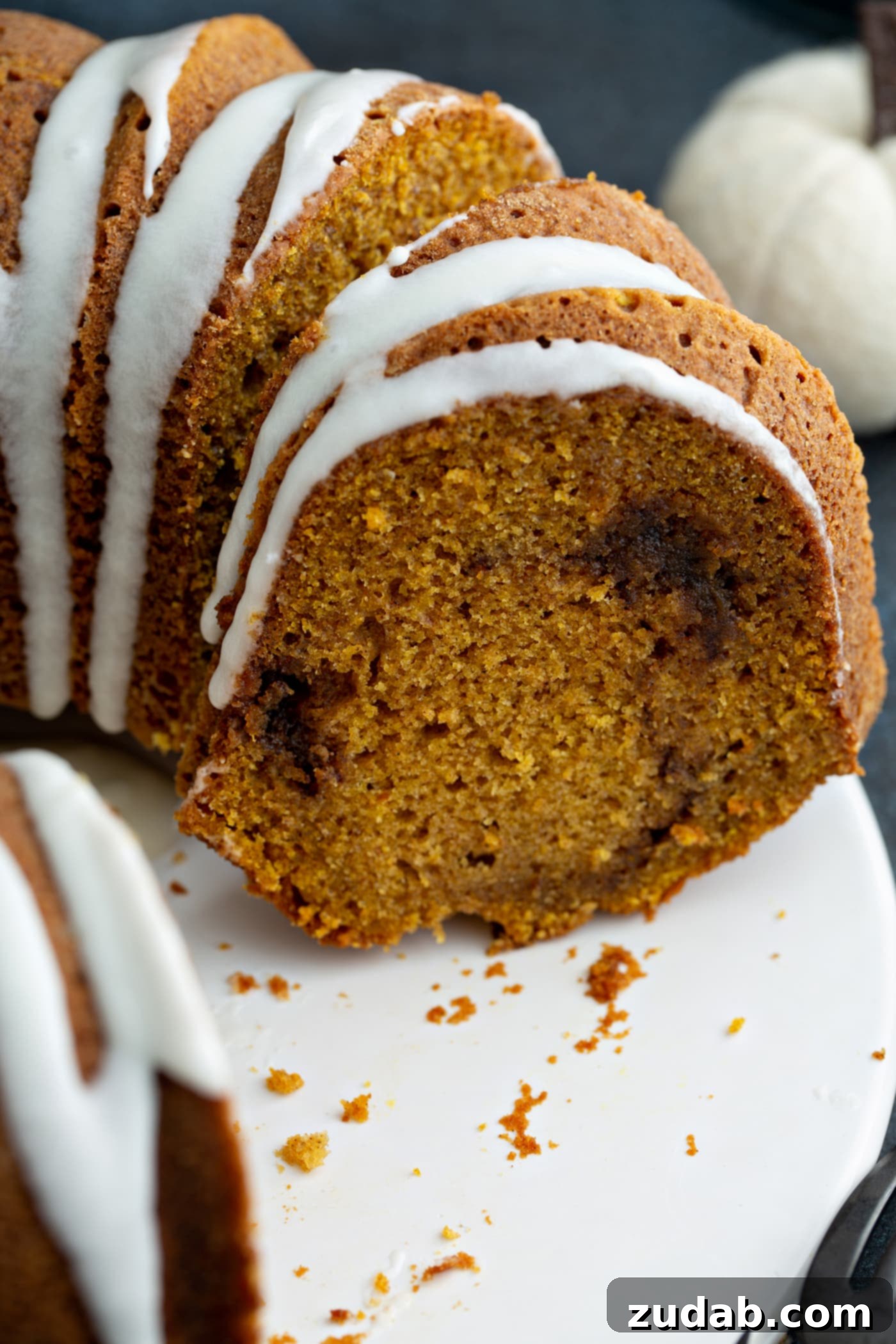 Sour Cream Cinnamon Swirl Pumpkin Bundt Cake A detailed close-up of a generous slice of Sour Cream Cinnamon Swirl Pumpkin Bundt Cake, showcasing the delicate white glaze drizzled over its golden-brown surface and the distinct, inviting cinnamon swirl embedded in the moist pumpkin cake interior.