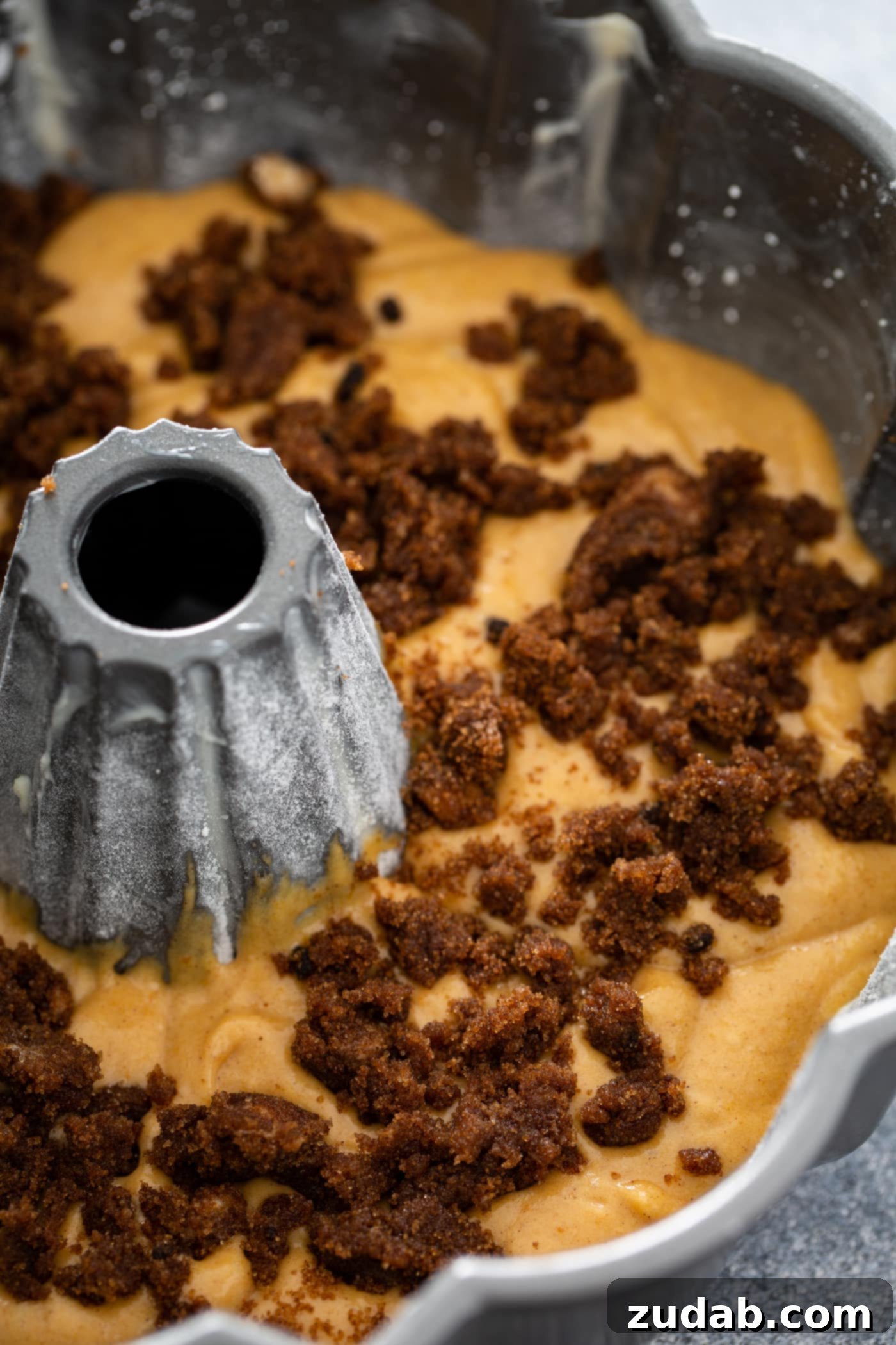 Sour Cream Cinnamon Swirl Pumpkin Bundt Cake An unbaked pumpkin bundt cake, still in its bundt pan, revealing a generous layer of cinnamon filling artfully placed on top of the first layer of batter, ready for the final layer and baking.