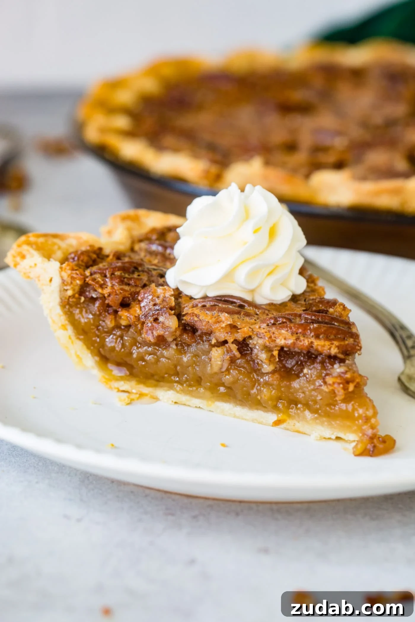 A photo of a slice of pecan pie sitting on a white place with a dollop of whipped cream on top.