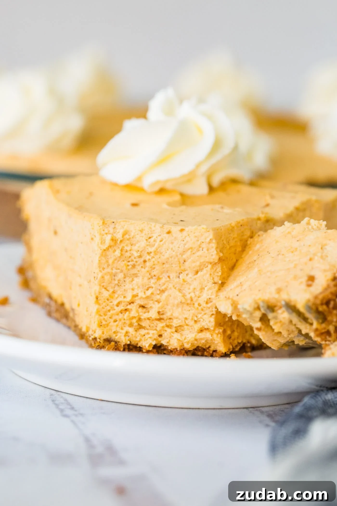 Marshmallow No Bake Pumpkin Pie A photo of a slice of no bake pumpkin pie sitting on a white plate with a bite-size piece removed with a fork, showcasing its creamy texture.
