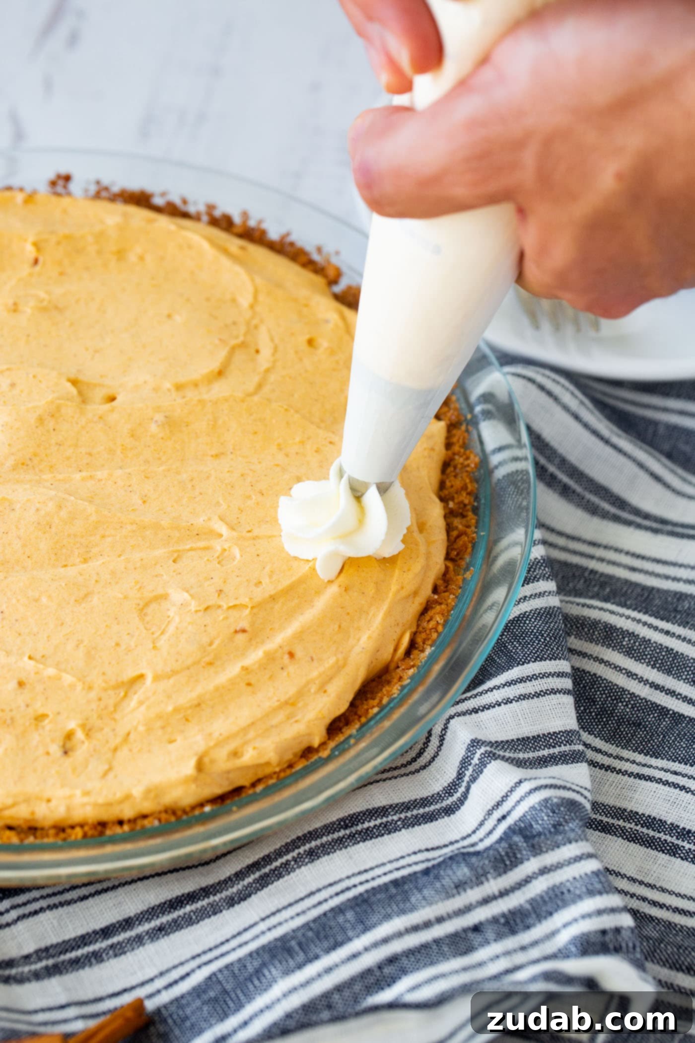 Marshmallow No Bake Pumpkin Pie A photo of a no bake pumpkin pie with beautiful swirls of whipped cream being piped on top, ready for a finishing touch.