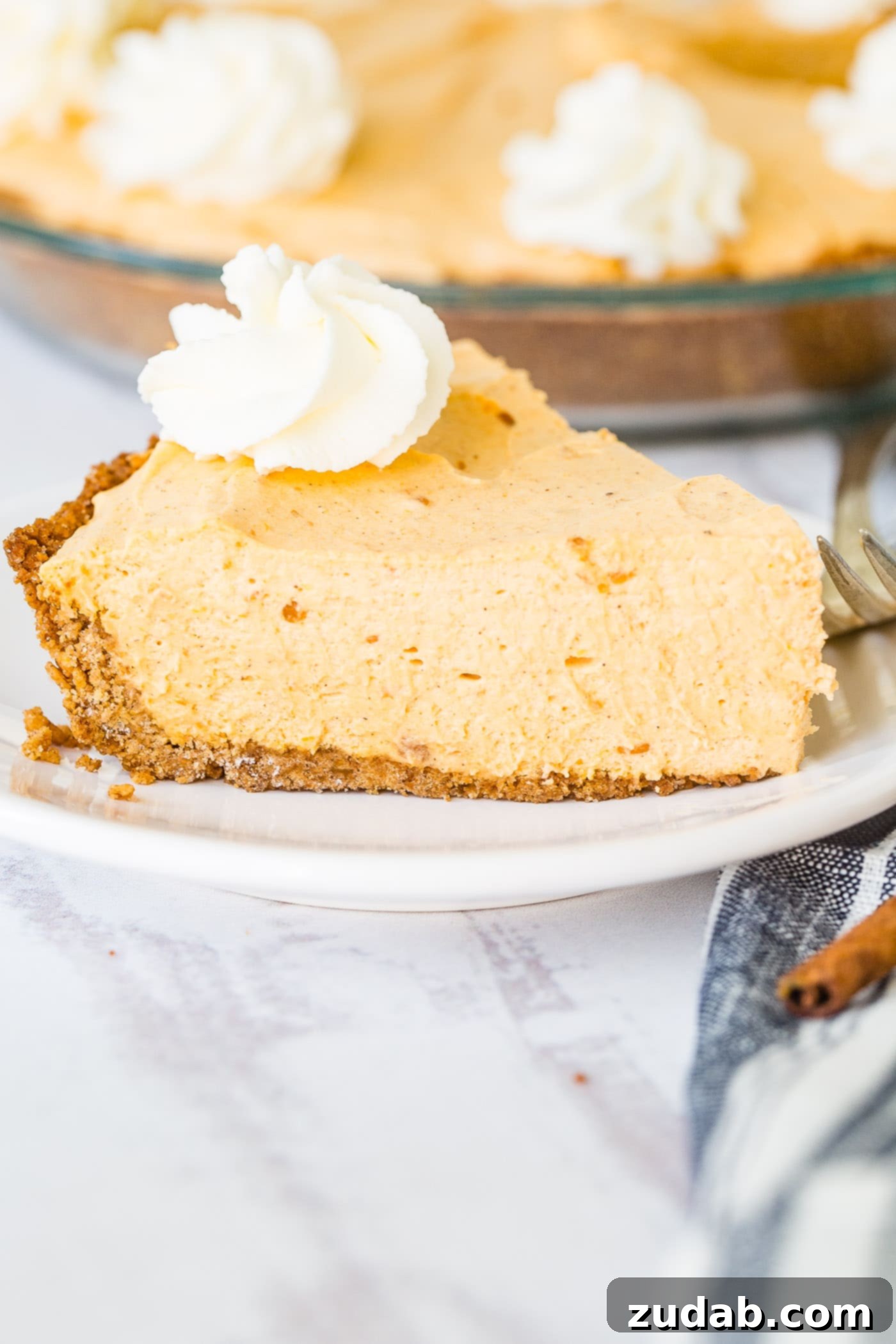 Marshmallow No Bake Pumpkin Pie A photo of a slice of no bake pumpkin pie on a white plate with a swirl of whipped cream on top, inviting dessert lovers.