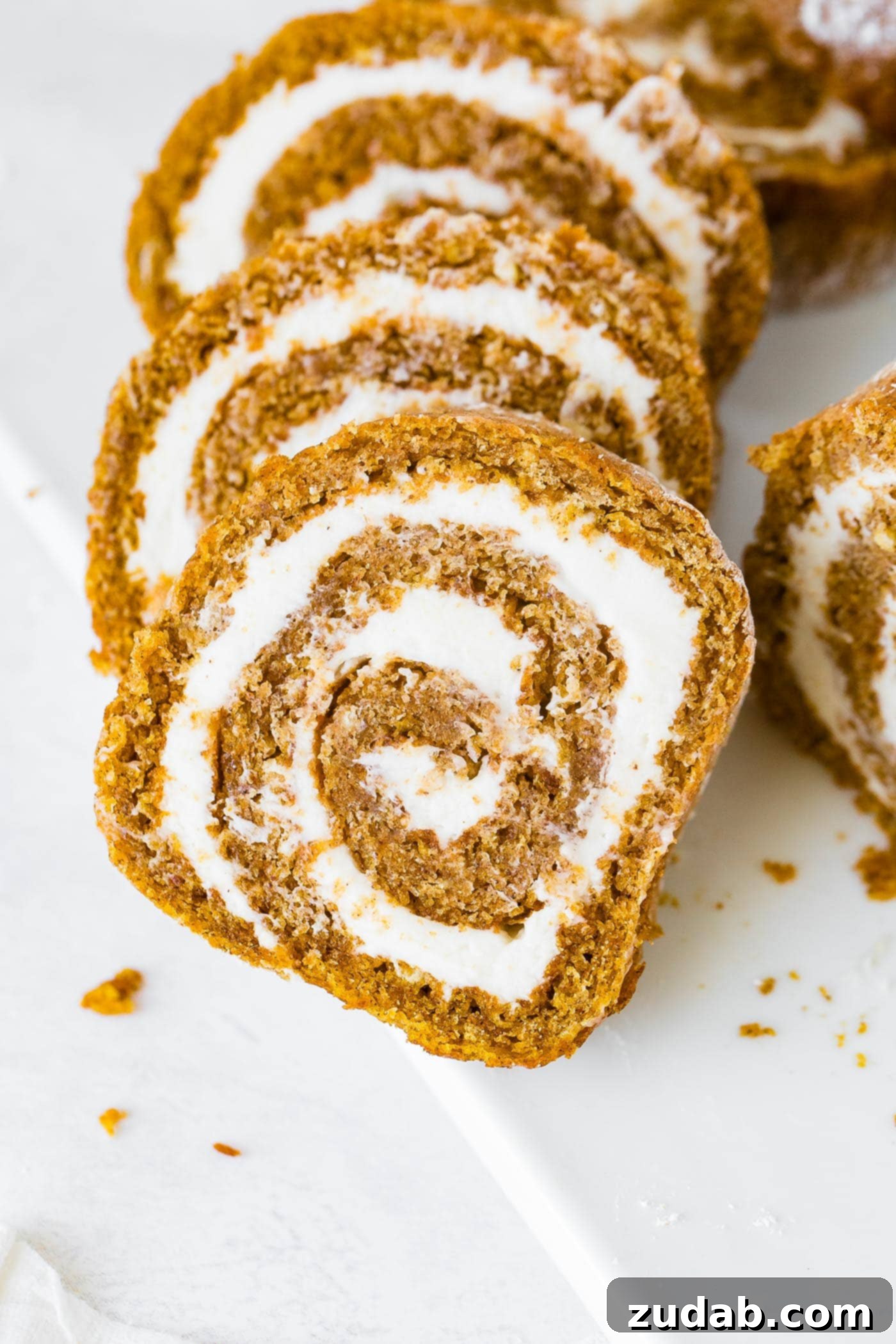 Better Than Libby's Pumpkin Roll Recipe A photo of several slices of pumpkin roll with cream cheese frosting, ready to be served.