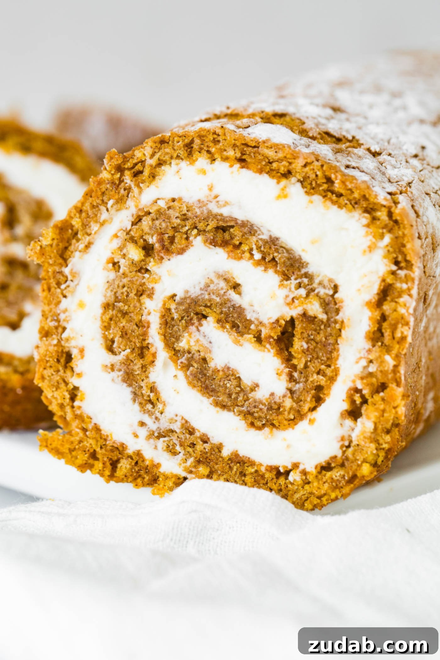 Better Than Libby's Pumpkin Roll Recipe A photo of a cross-section of a perfectly rolled pumpkin roll with swirls of cream cheese filling.