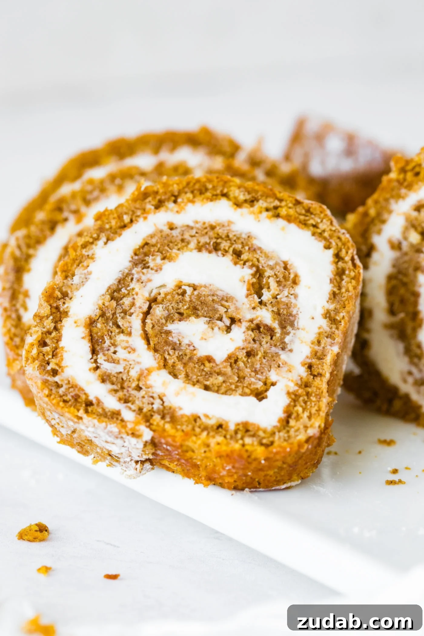 Better Than Libby's Pumpkin Roll Recipe A photo of several slices of pumpkin roll with cream cheese frosting, artfully arranged on a serving platter.