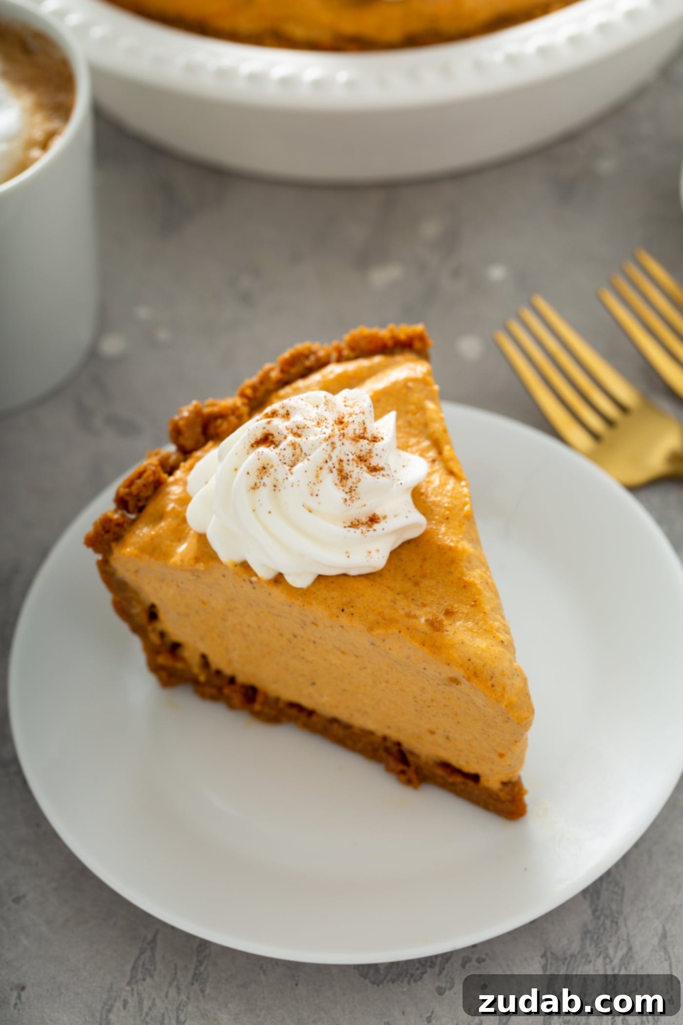 A single slice of pumpkin ice cream pie, beautifully presented on a white dessert plate. The pie is crowned with a dollop of whipped cream, delicately sprinkled with cinnamon. Two forks are placed neatly beside the plate on the table, inviting someone to indulge.