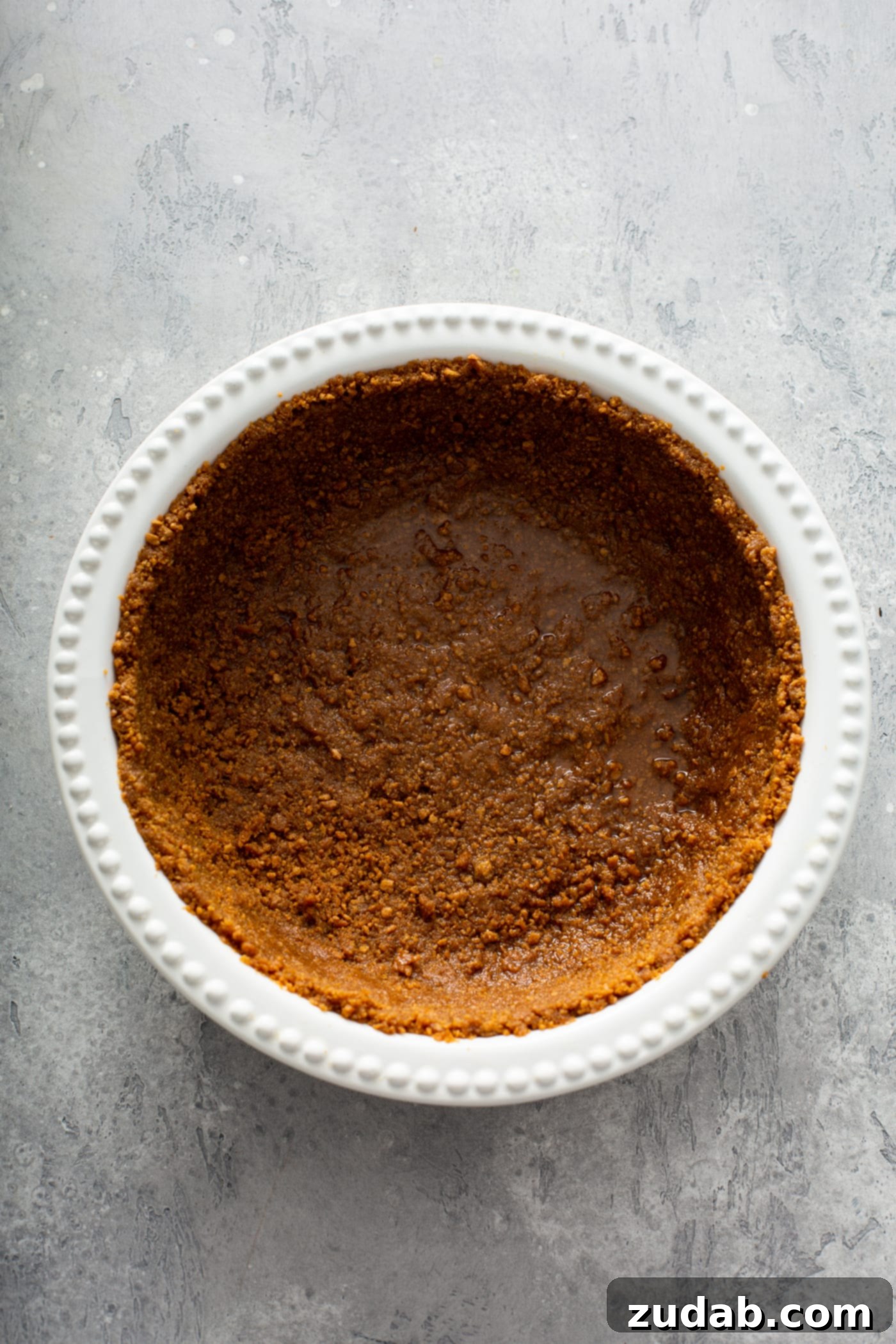 A pristine white pie dish holds a perfectly formed gingersnap crust, golden-brown and ready for its creamy filling.