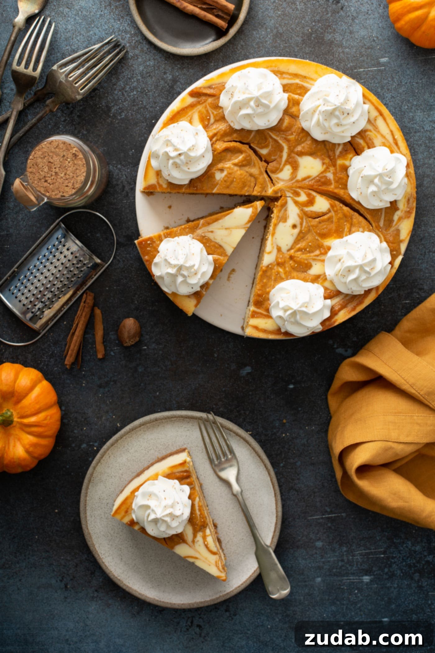 Swirled Pumpkin Cheesecake A dessert plate displays a single slice of swirled pumpkin cheesecake, accompanied by a fork. In the background, the remaining whole cheesecake is visible, along with decorative cinnamon sticks, a small pumpkin, and a neatly folded orange napkin, setting a cozy fall scene.