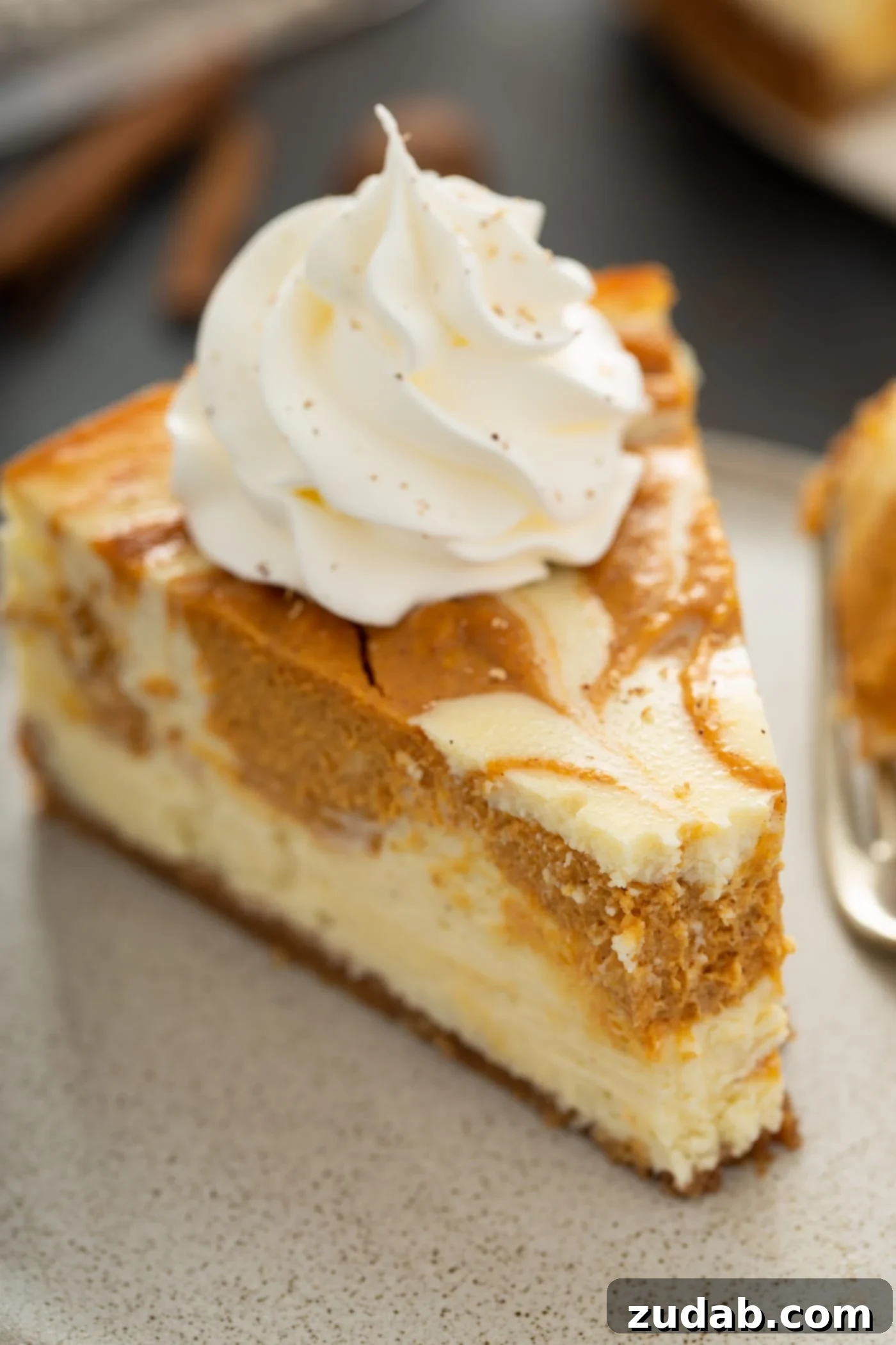 Swirled Pumpkin Cheesecake A dessert plate holds a slice of swirled pumpkin cheesecake, topped with a dollop of whipped cream, with a small bite already taken from its tip, revealing its creamy layers.