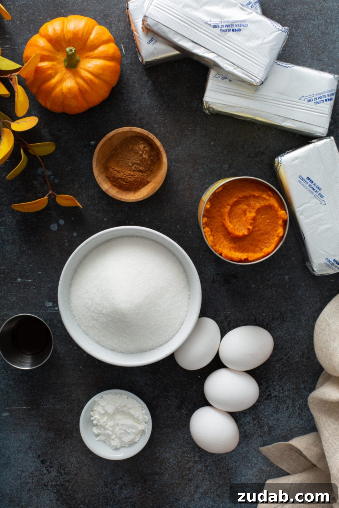 Swirled Pumpkin Cheesecake A collection of fresh ingredients laid out for the swirled pumpkin cheesecake: bowls of granulated sugar, fresh eggs, a can of pure pumpkin, ground cinnamon, softened cream cheese, and a bottle of vanilla extract.