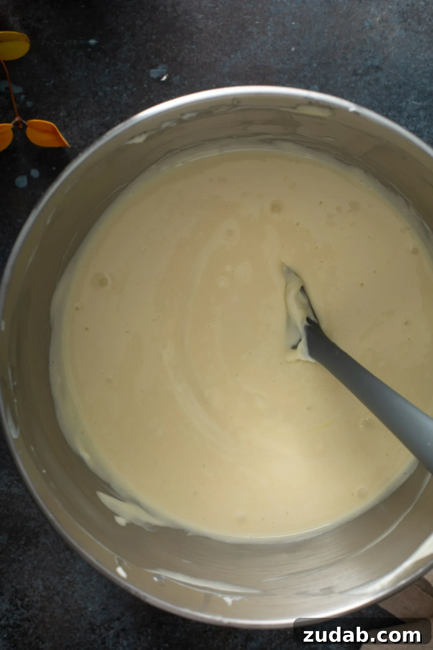Swirled Pumpkin Cheesecake A bowl filled with a smooth, pale cheesecake filling, with a spoon partially submerged in the creamy mixture, indicating it's ready for the next step.
