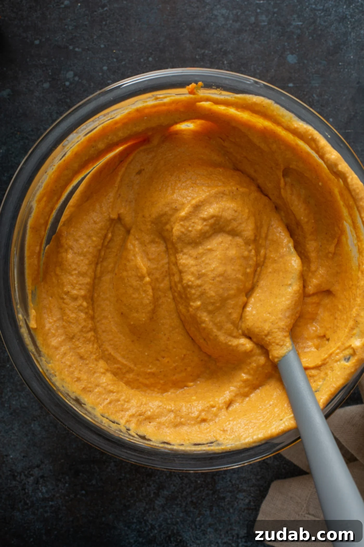 Swirled Pumpkin Cheesecake A bowl of creamy, orange-hued pumpkin cheesecake filling, perfectly mixed and ready for swirling, with a spoon resting inside.