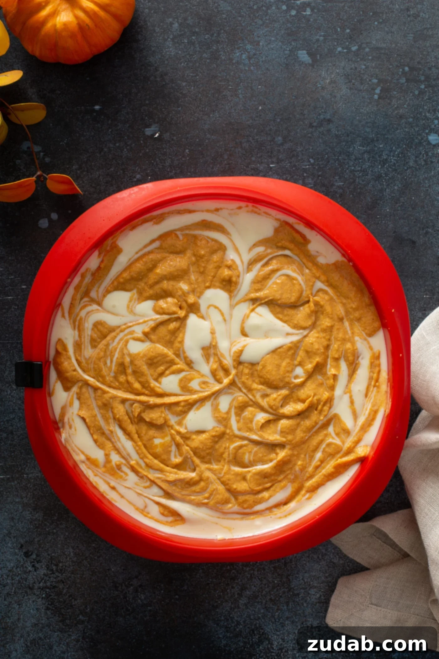 Swirled Pumpkin Cheesecake A close-up view of the cheesecake mixture in its springform pan, showcasing the intricate and appealing swirls of plain and pumpkin cheesecake batters beautifully blended together.