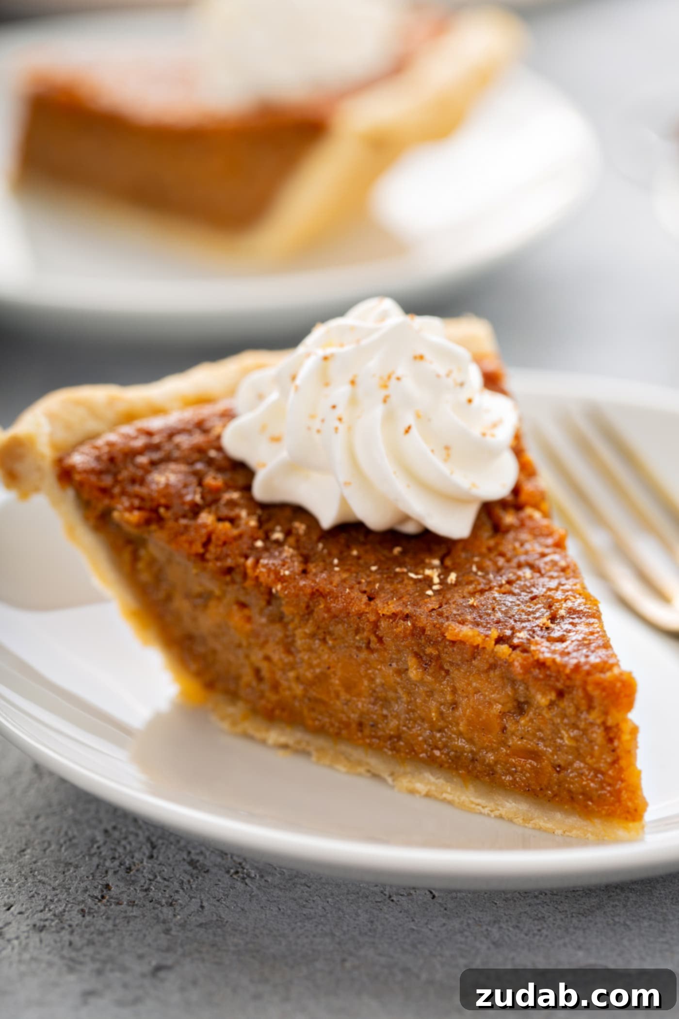 Perfectly Southern Sweet Potato Pie A photo of a slice of sweet potato pie with a dollop of whipped cream on top sitting on a white plate.