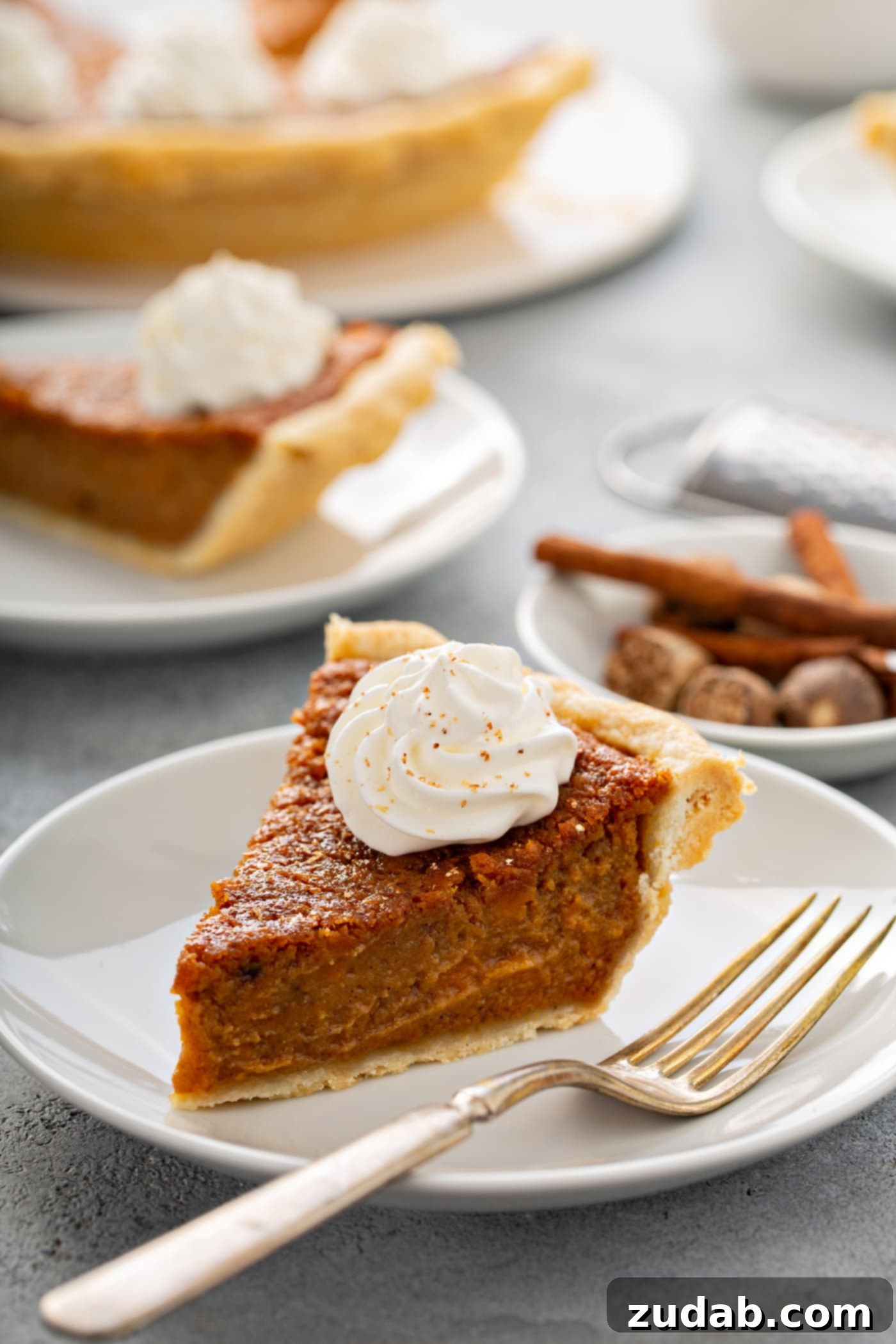 Perfectly Southern Sweet Potato Pie A photo of a slice of sweet potato pie sitting on a white plate with a fork sitting next to it and other servings of pie in the background.