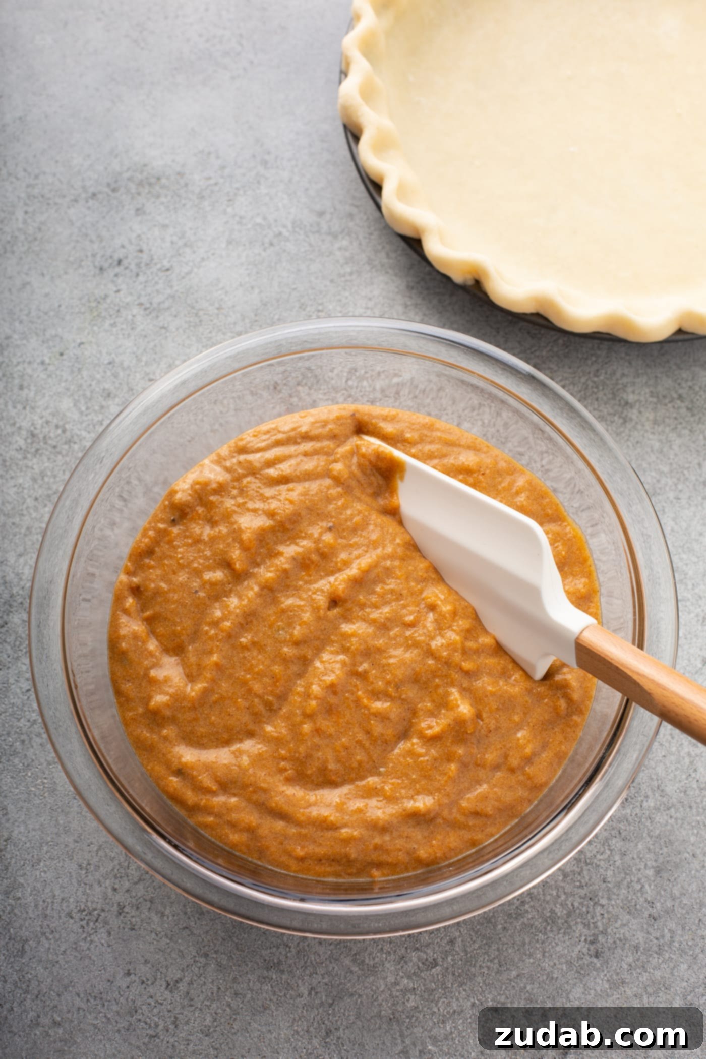 Perfectly Southern Sweet Potato Pie A photo of a glass bowl full of sweet potato pie filling with a rubber spatula in it. The bowl is sitting next to an empty pie crust.