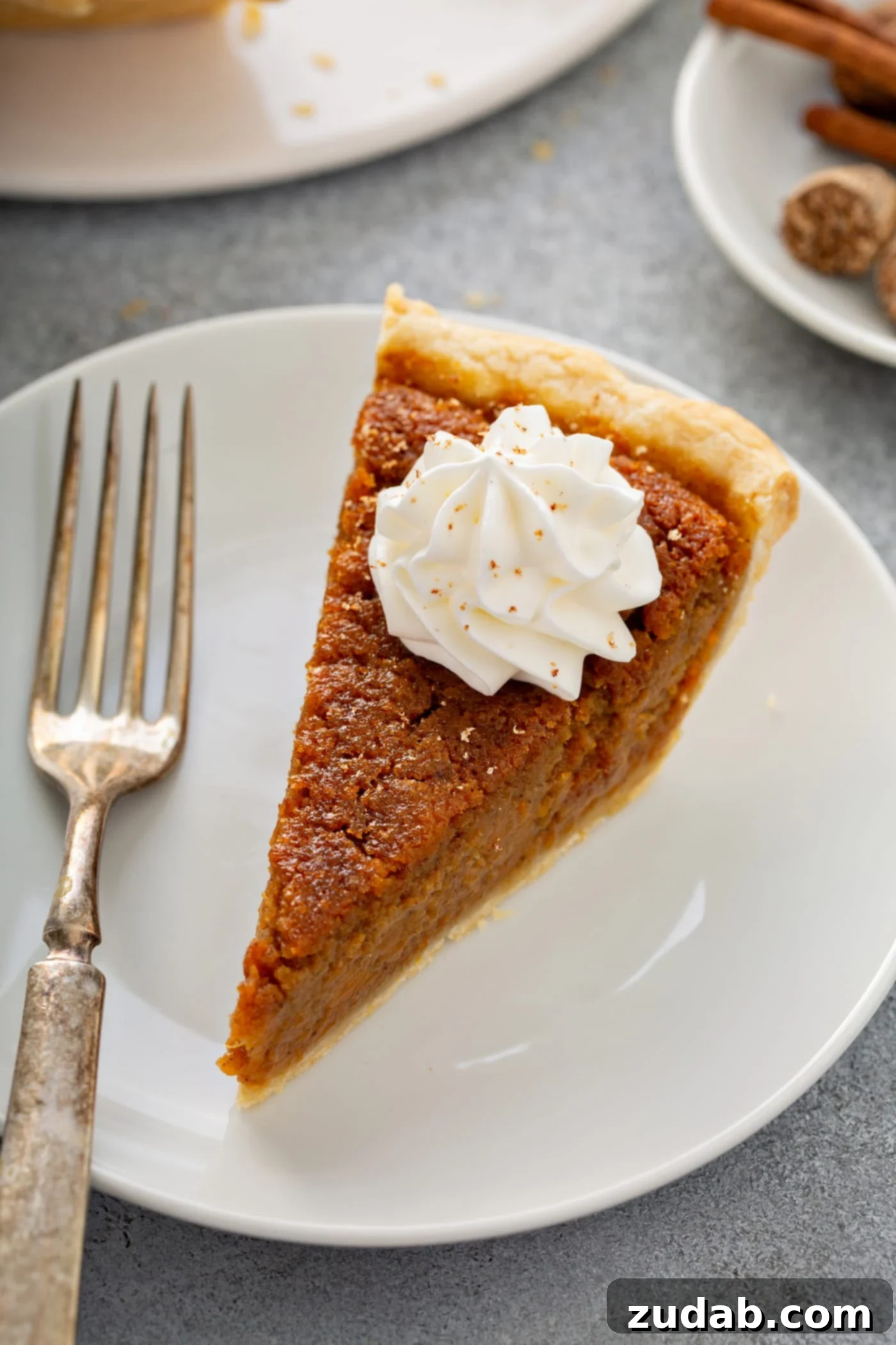 Perfectly Southern Sweet Potato Pie A photo of a slice of sweet potato pie sitting on a white plate with a silver fork sitting next to it.