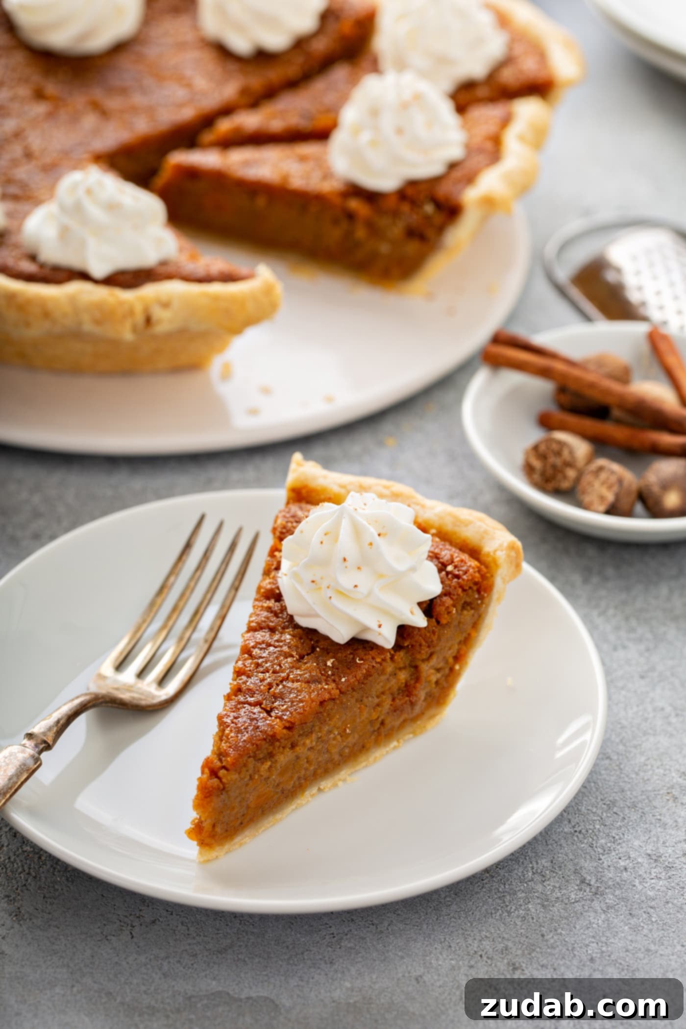 Perfectly Southern Sweet Potato Pie A photo of a slice of sweet potato pie sitting on a white plate with the whole sweet potato pie in the background.