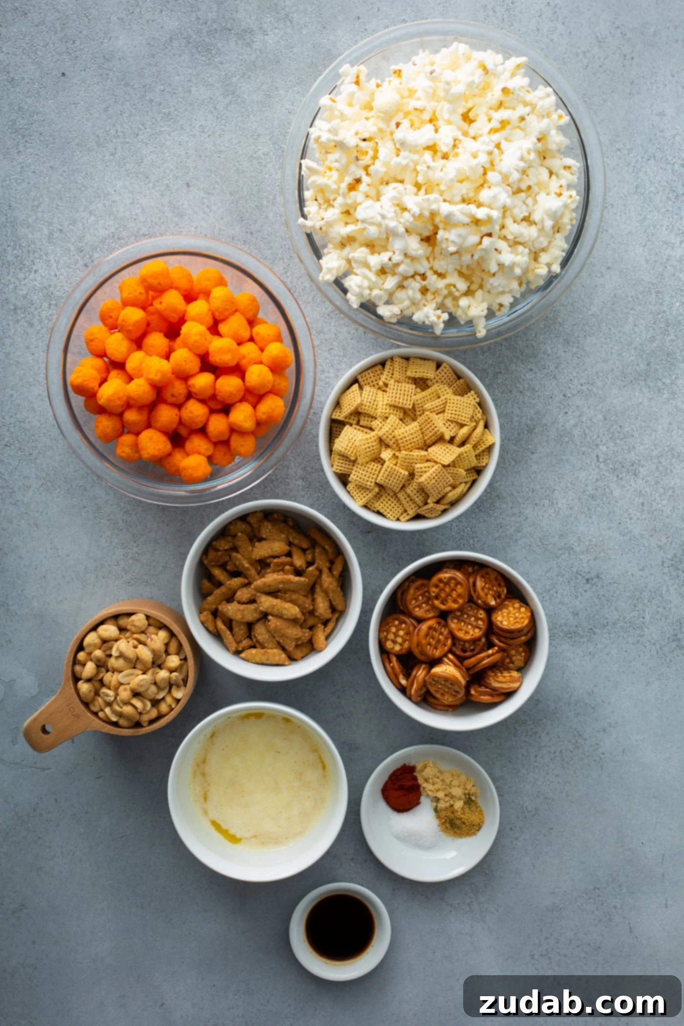 March Madness Snack Mix Containers of ingredients for a savory snack mix. There is popcorn, cheese balls, pretzels, sesame sticks, peanuts and spices.